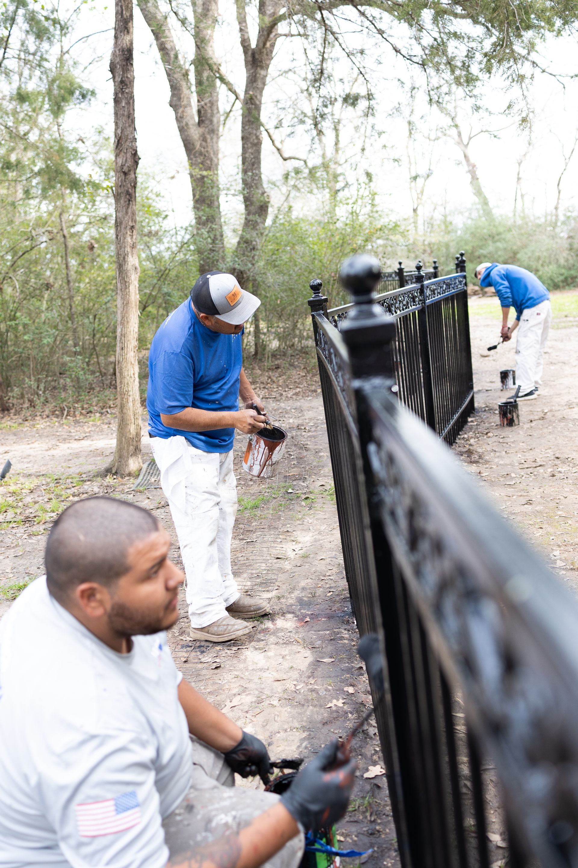 A group of men are painting a black fence.