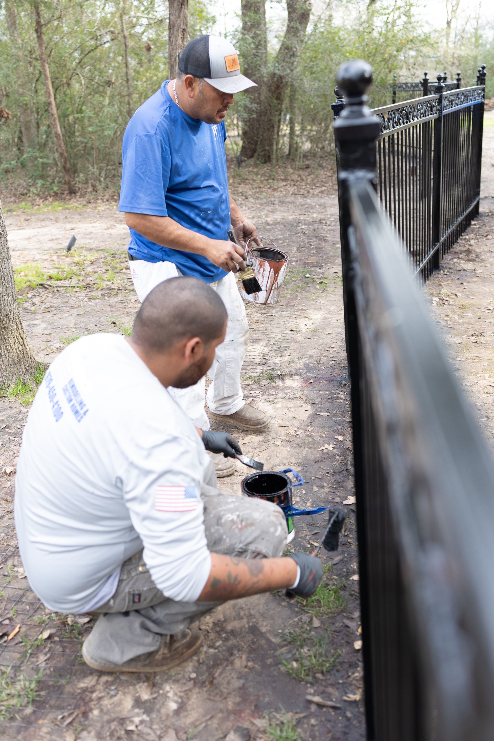 Two men are painting a fence in a park.