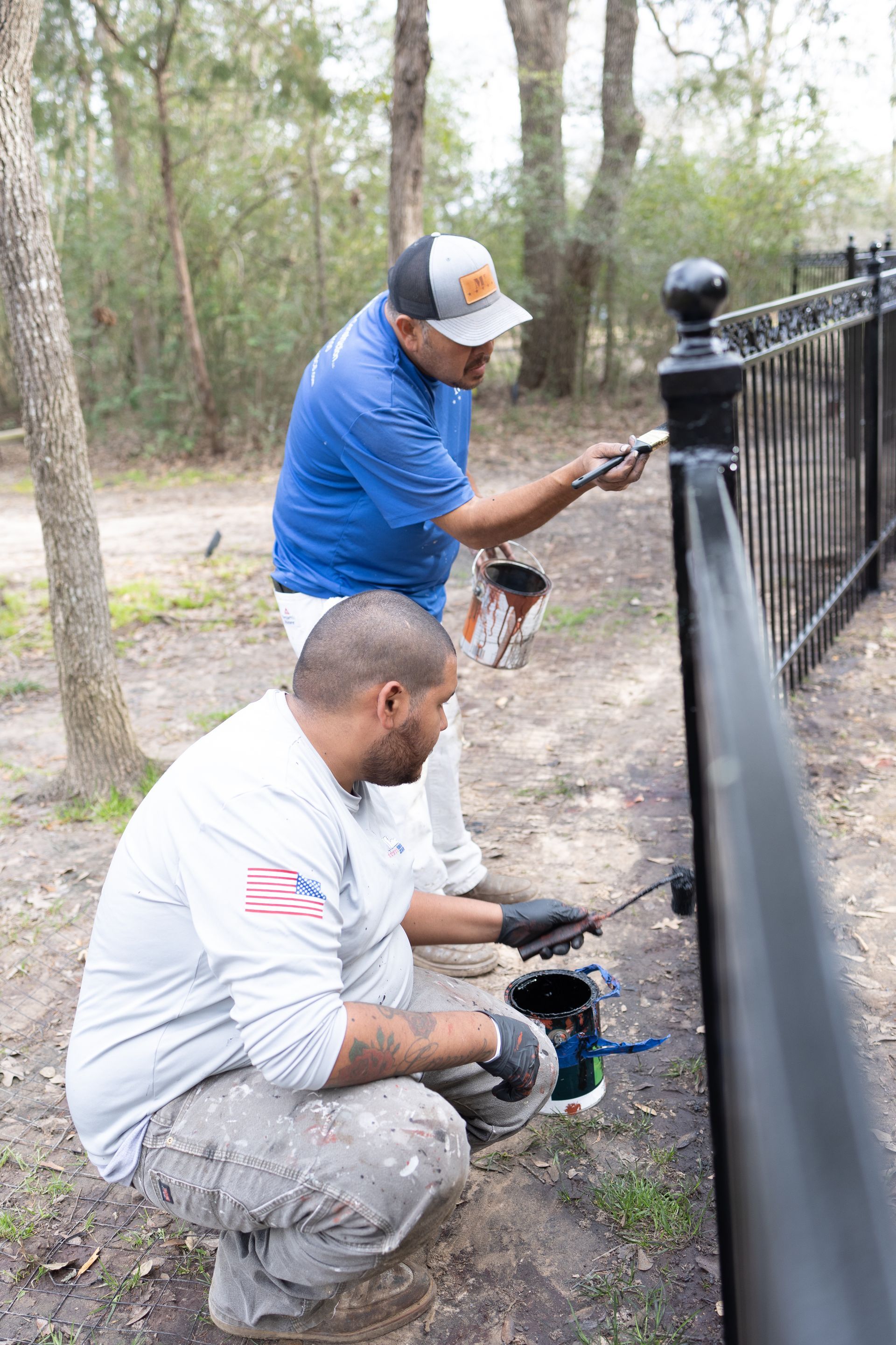 Two men are kneeling down and painting a metal fence.