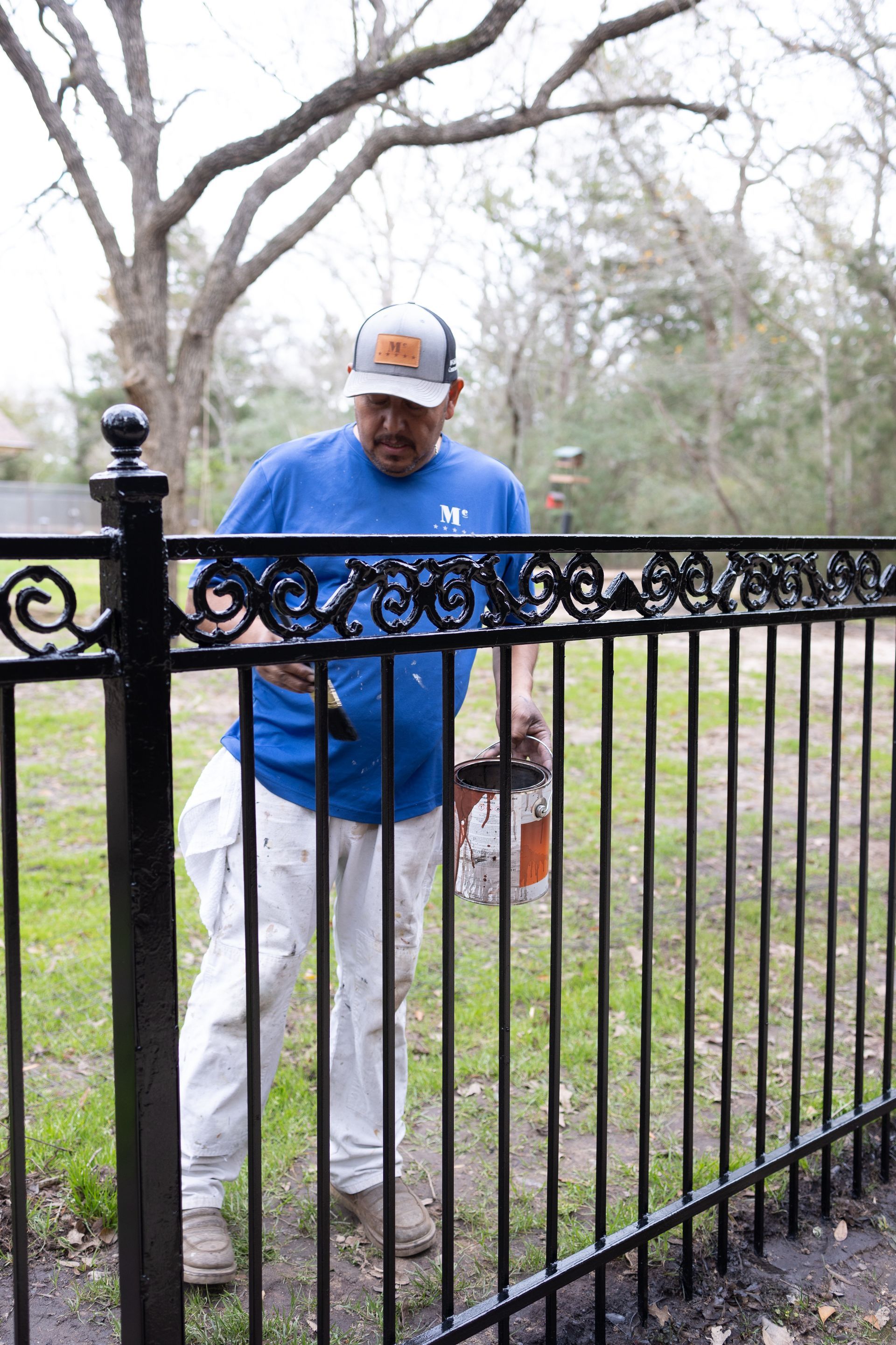 A man is painting a wrought iron fence in a yard.