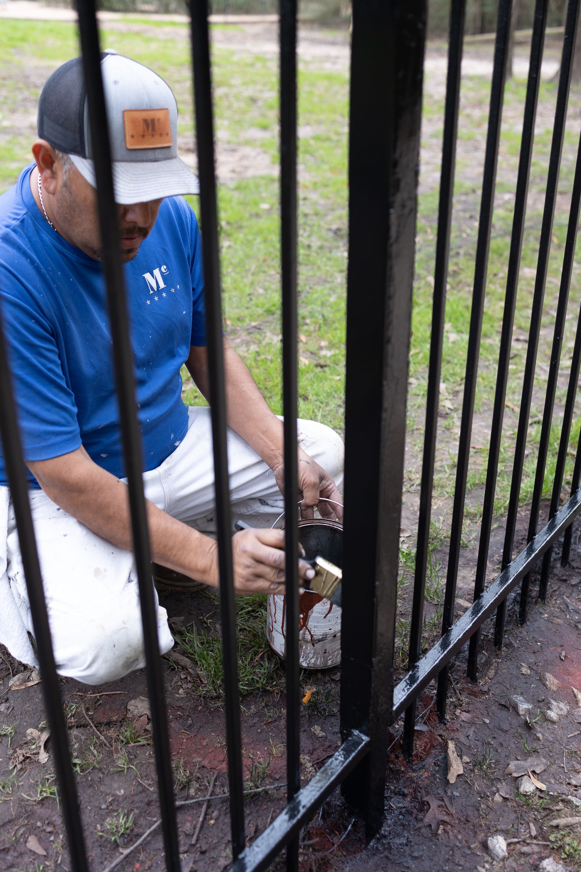 A man is kneeling down and painting a metal fence.