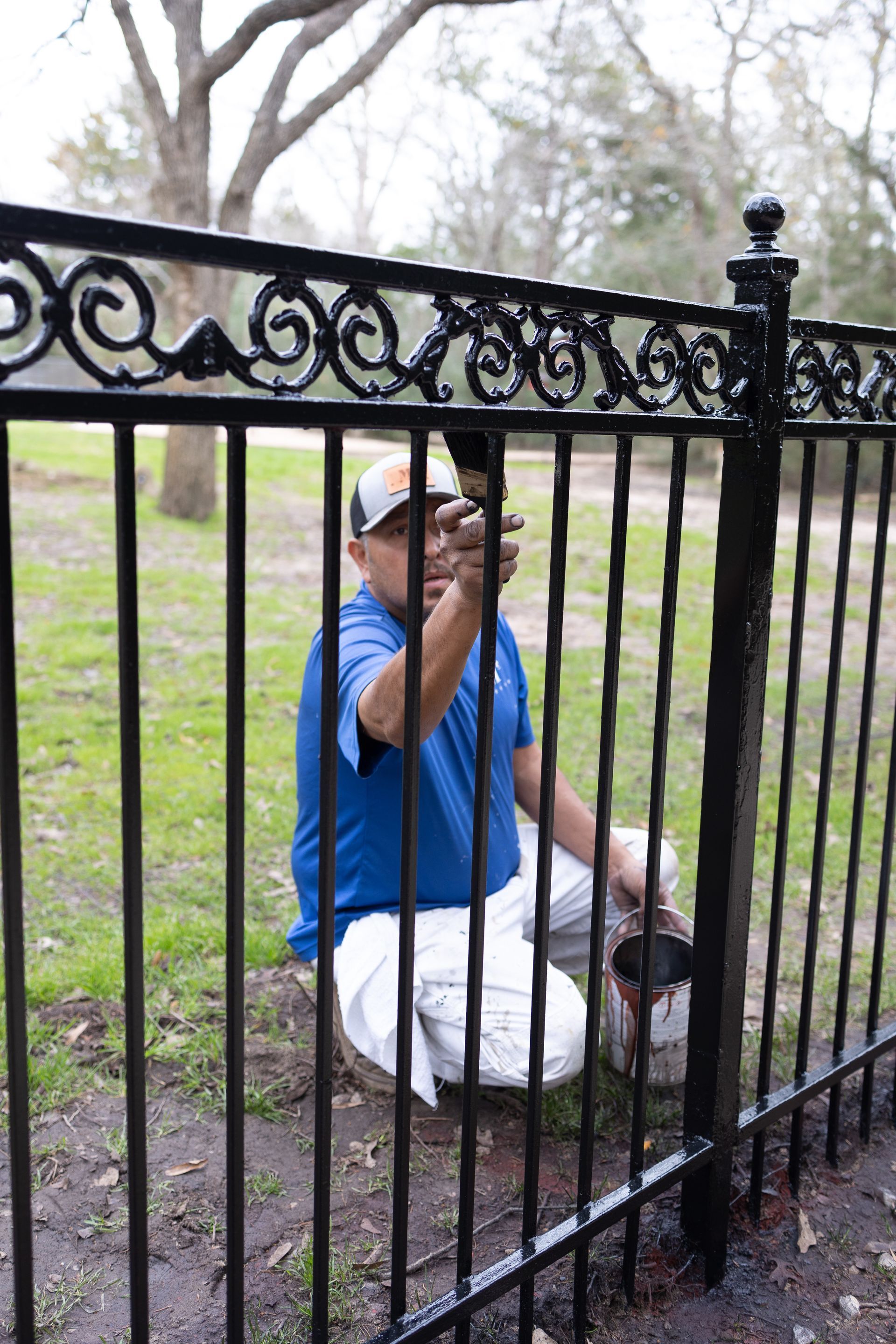 A man is kneeling down and painting a metal fence.