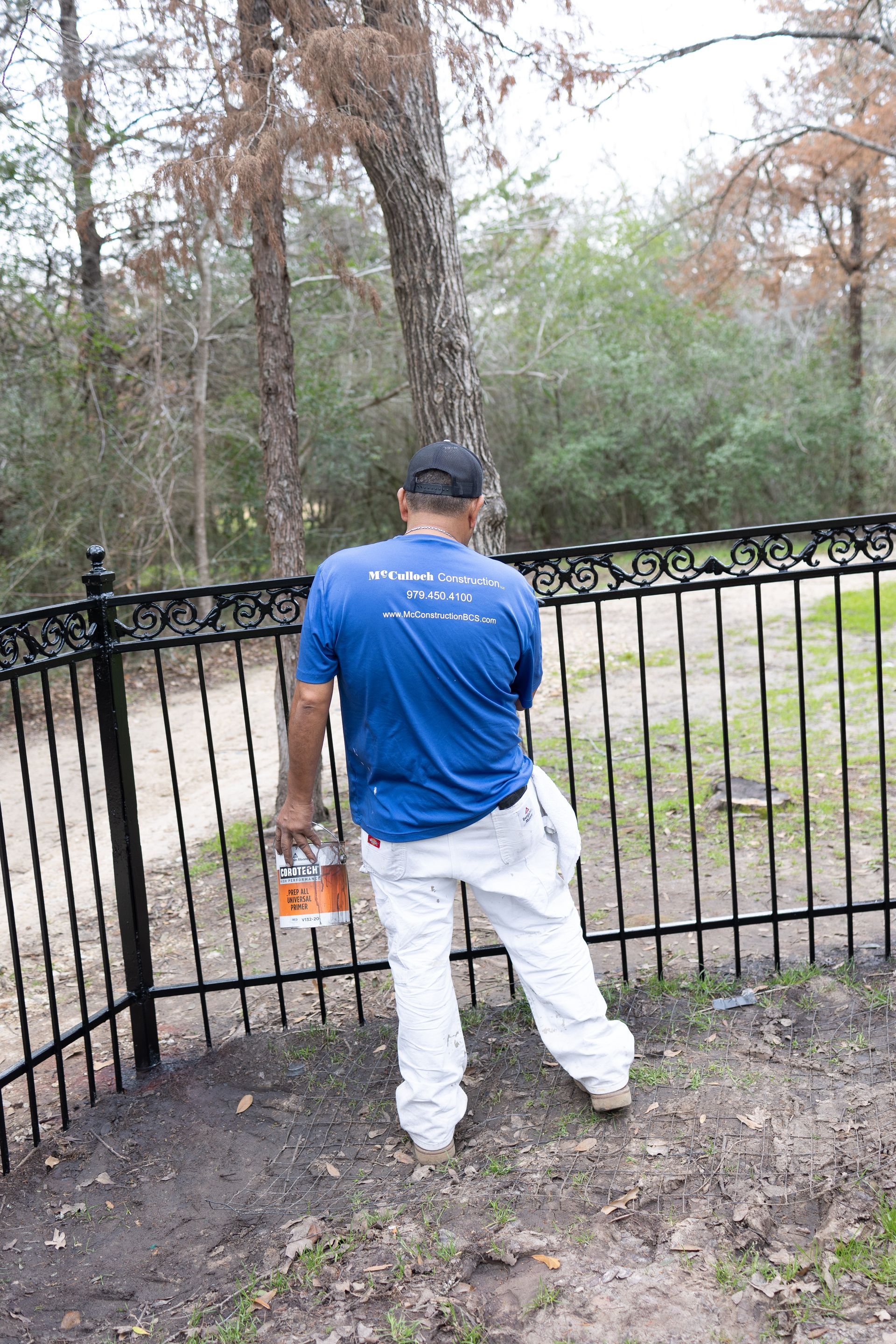 A man in a blue shirt and white pants is painting a fence.