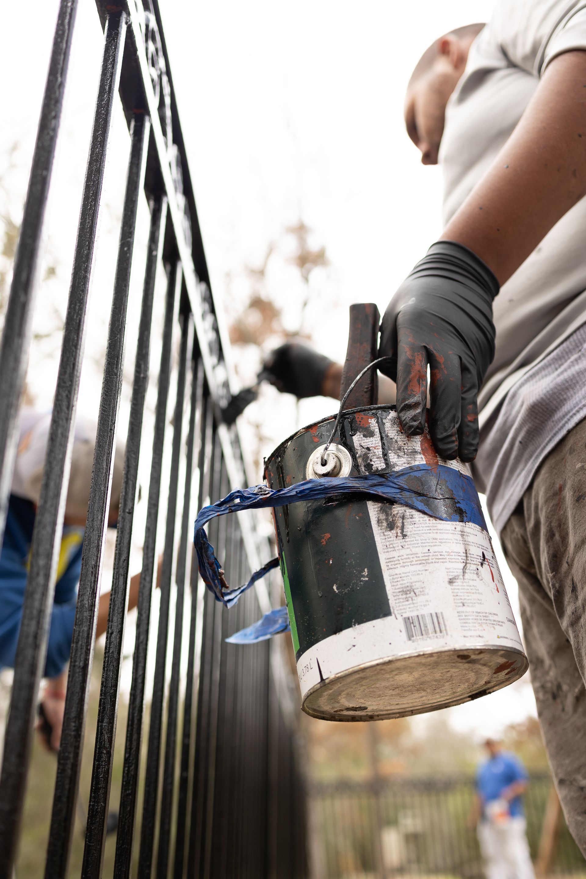 A man is holding a can of paint and painting a fence.