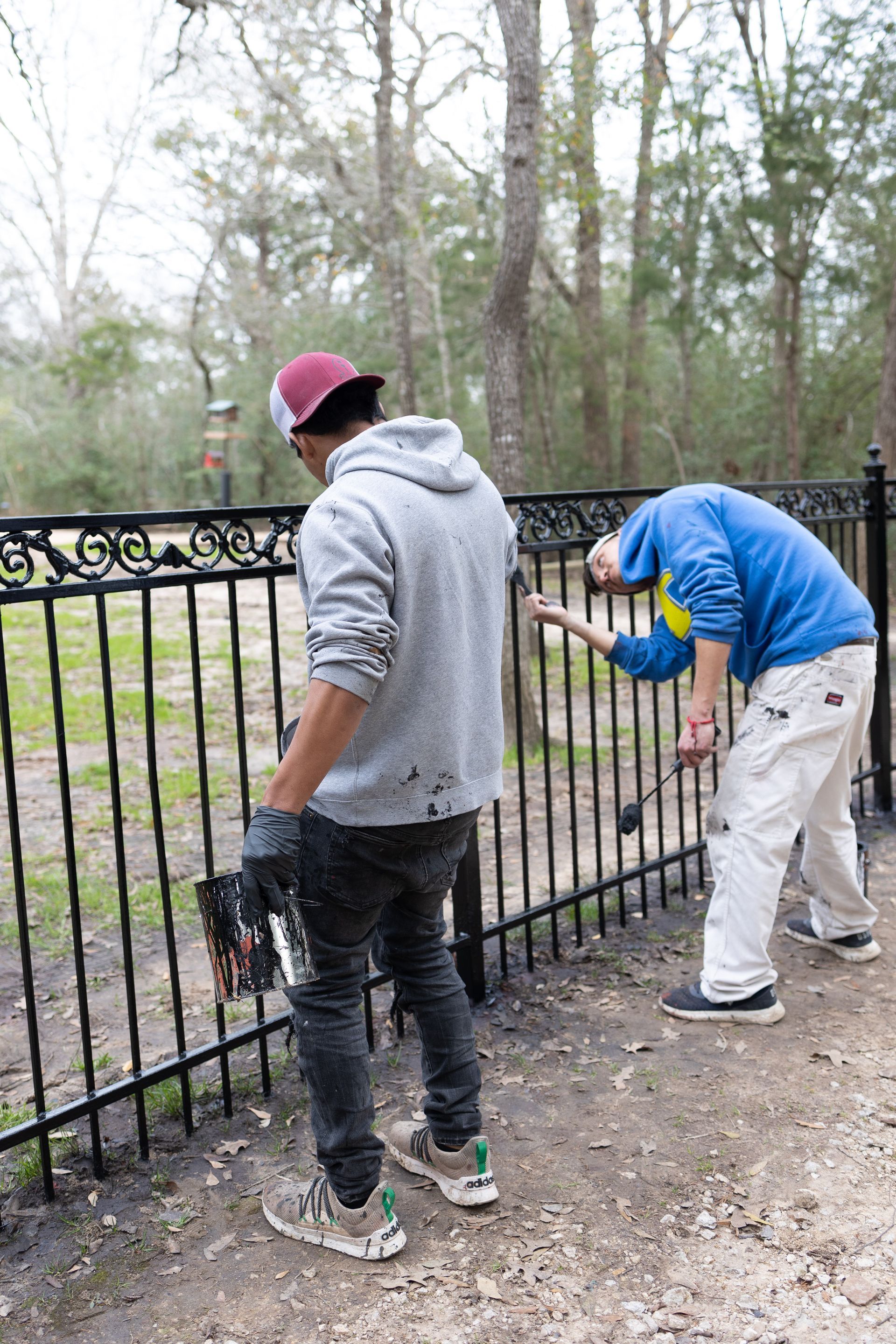 Two men are painting a metal fence in a park.