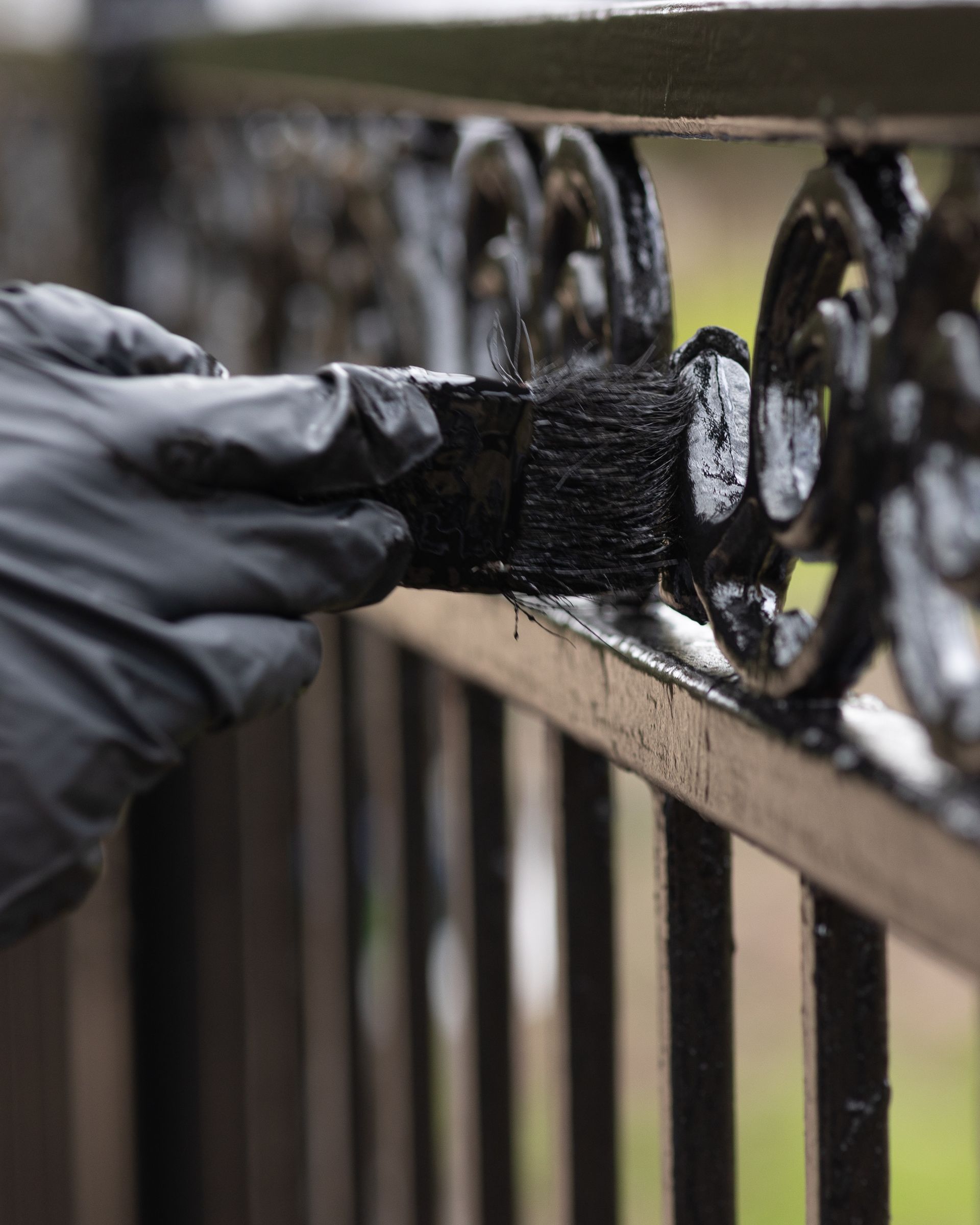 A person is painting a wrought iron fence with a brush.