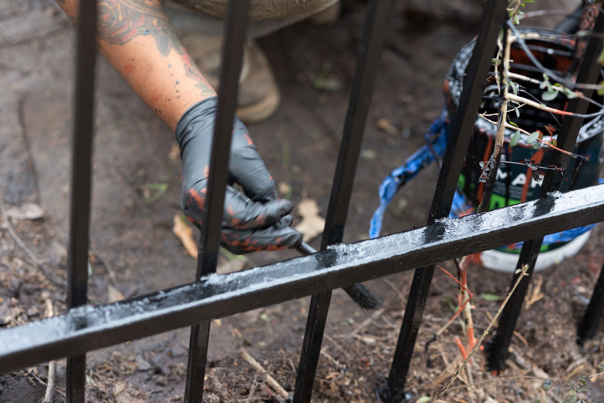 A person is painting a metal fence with a brush.