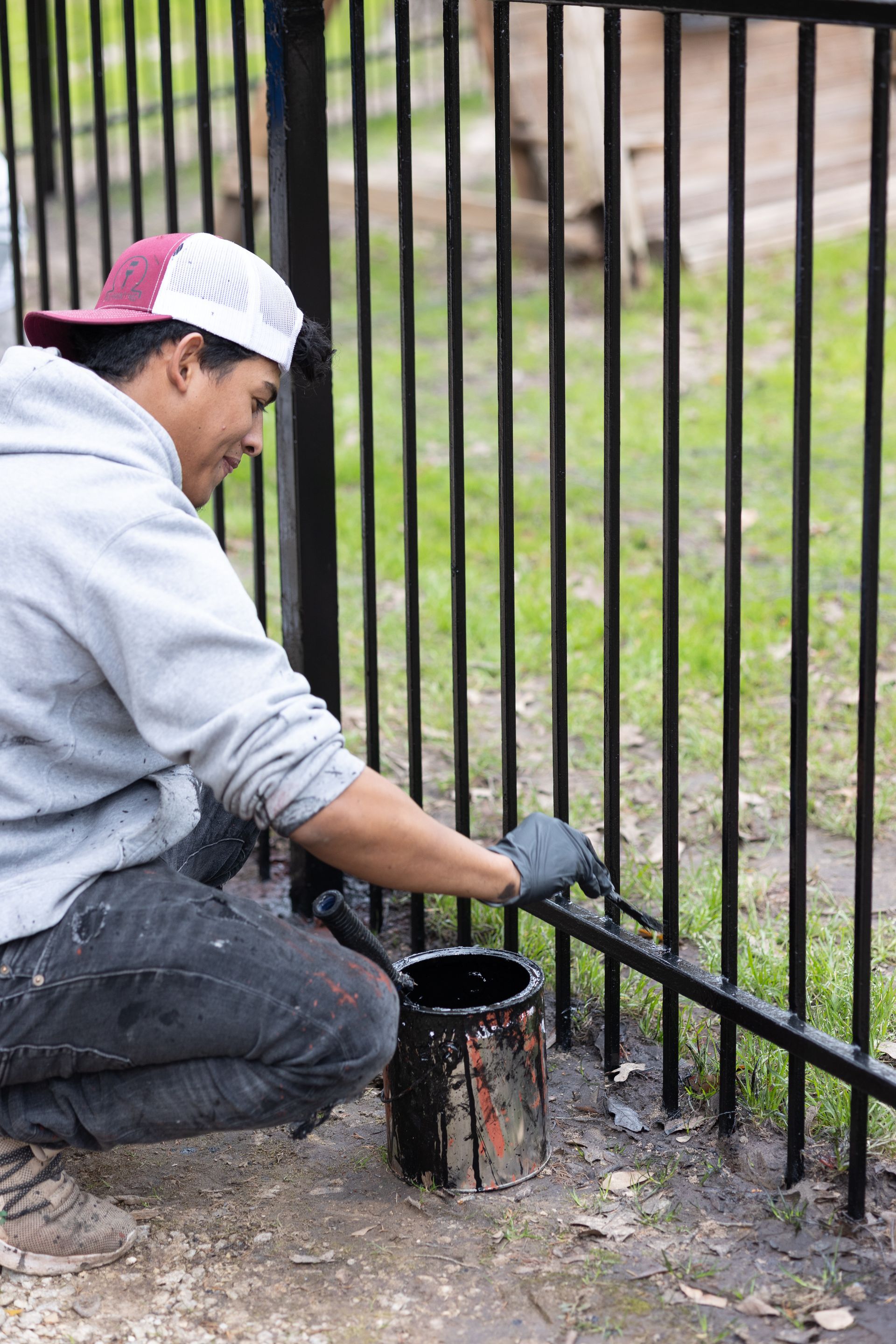 A man is kneeling down and painting a metal fence.