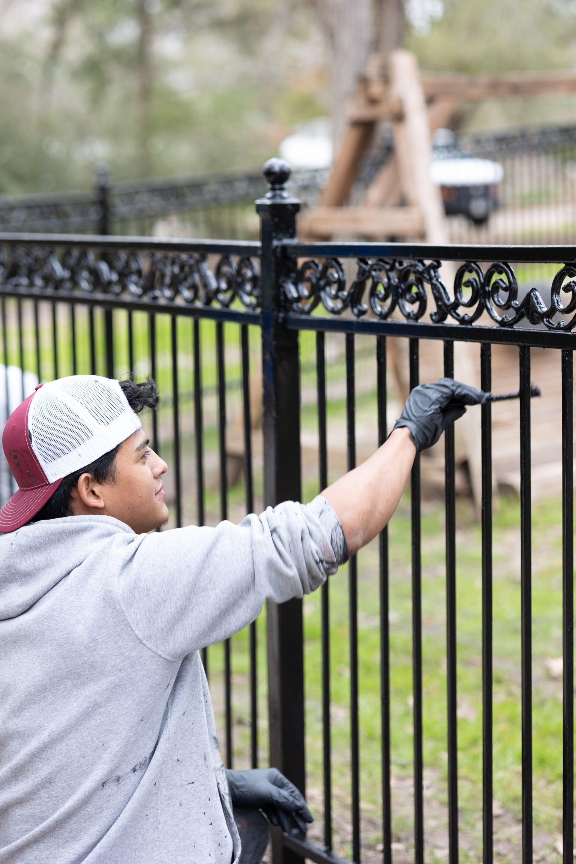 A man is painting a metal fence with a brush.