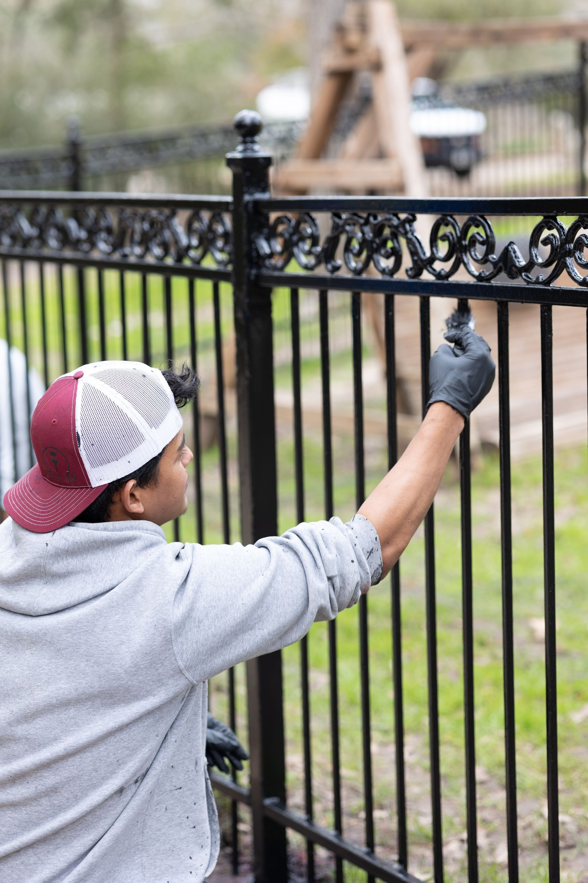 A man is painting a metal fence with a brush.