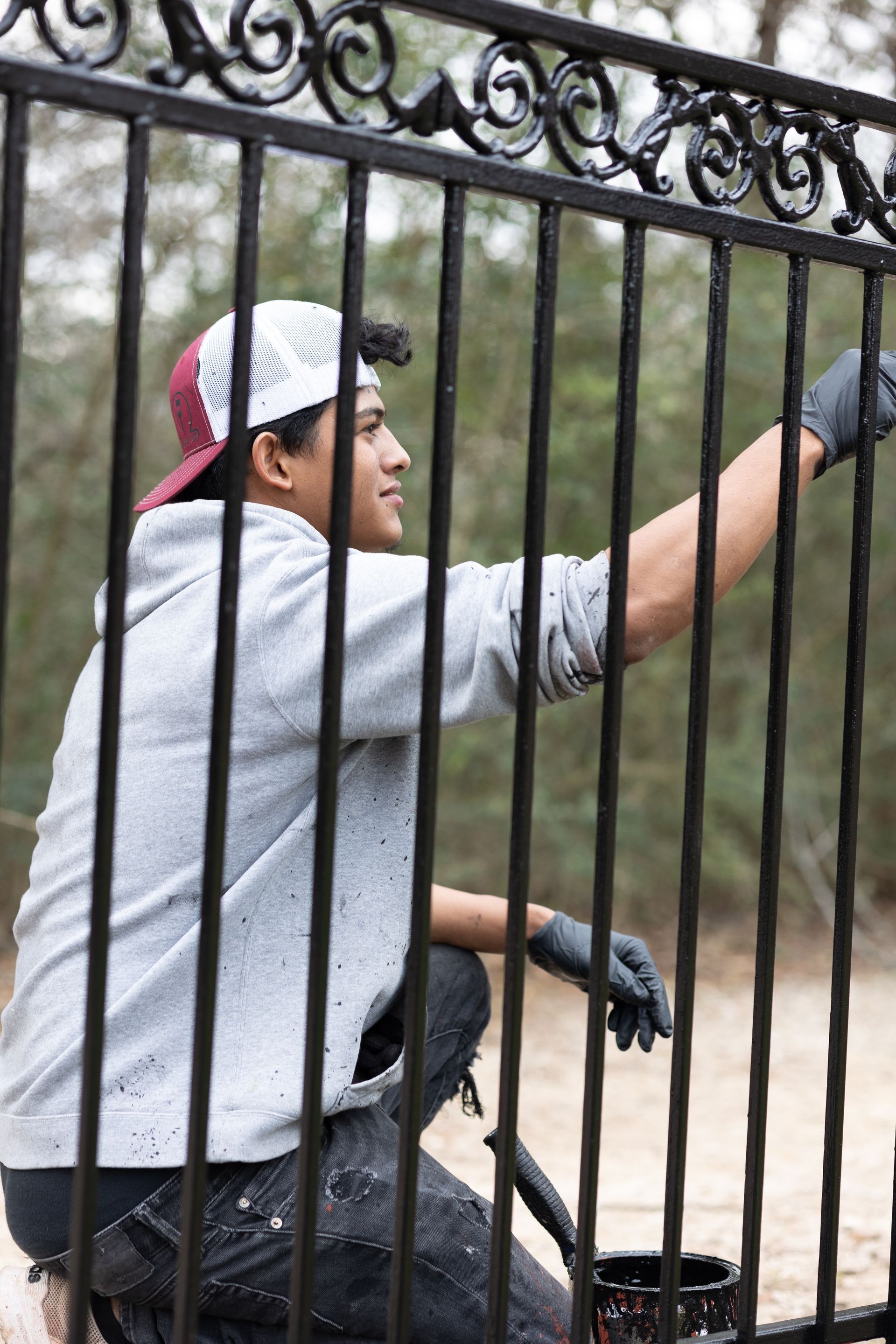 A man is painting a metal fence with a brush.