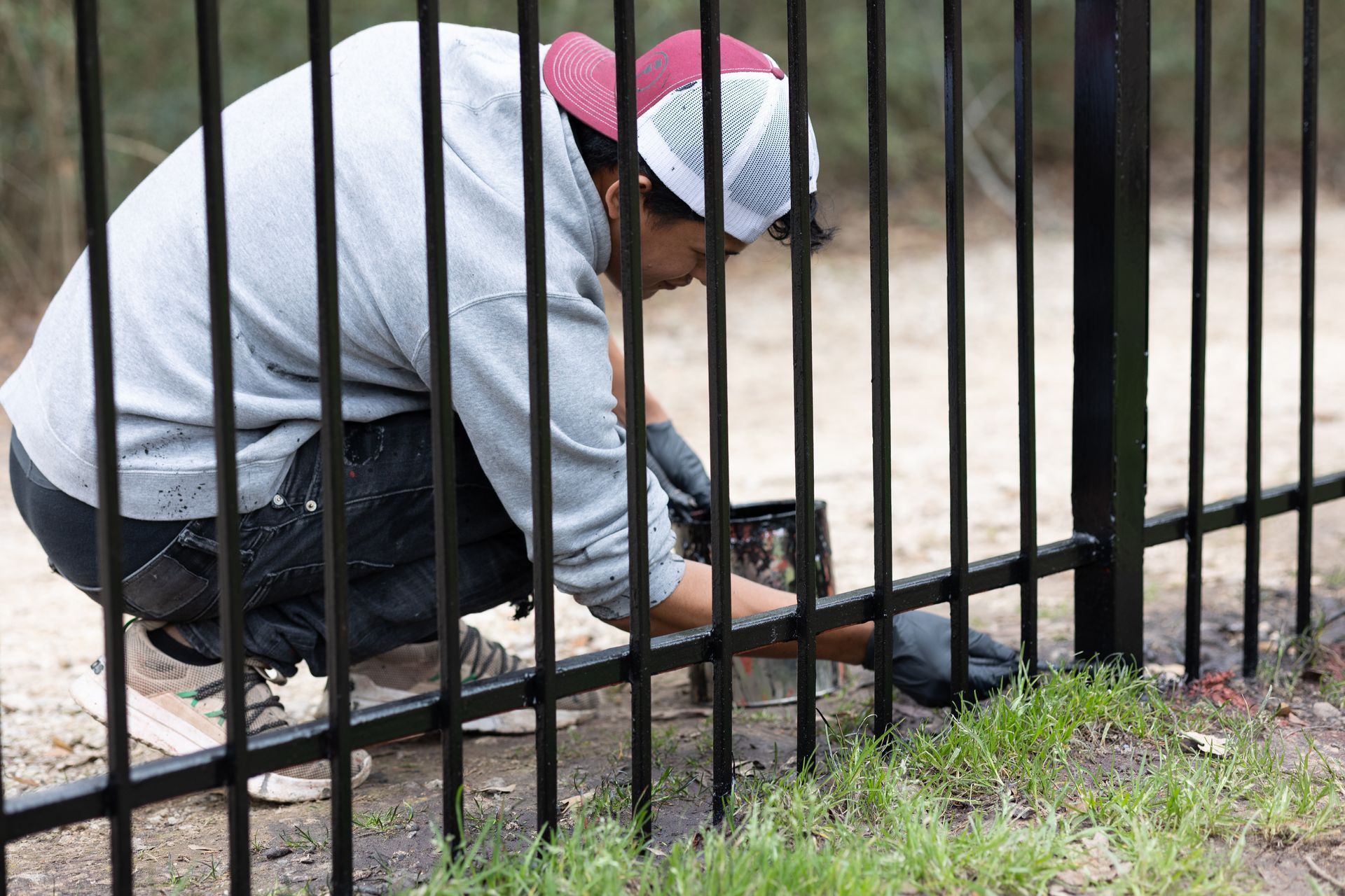 A man is kneeling down and working on a metal fence.