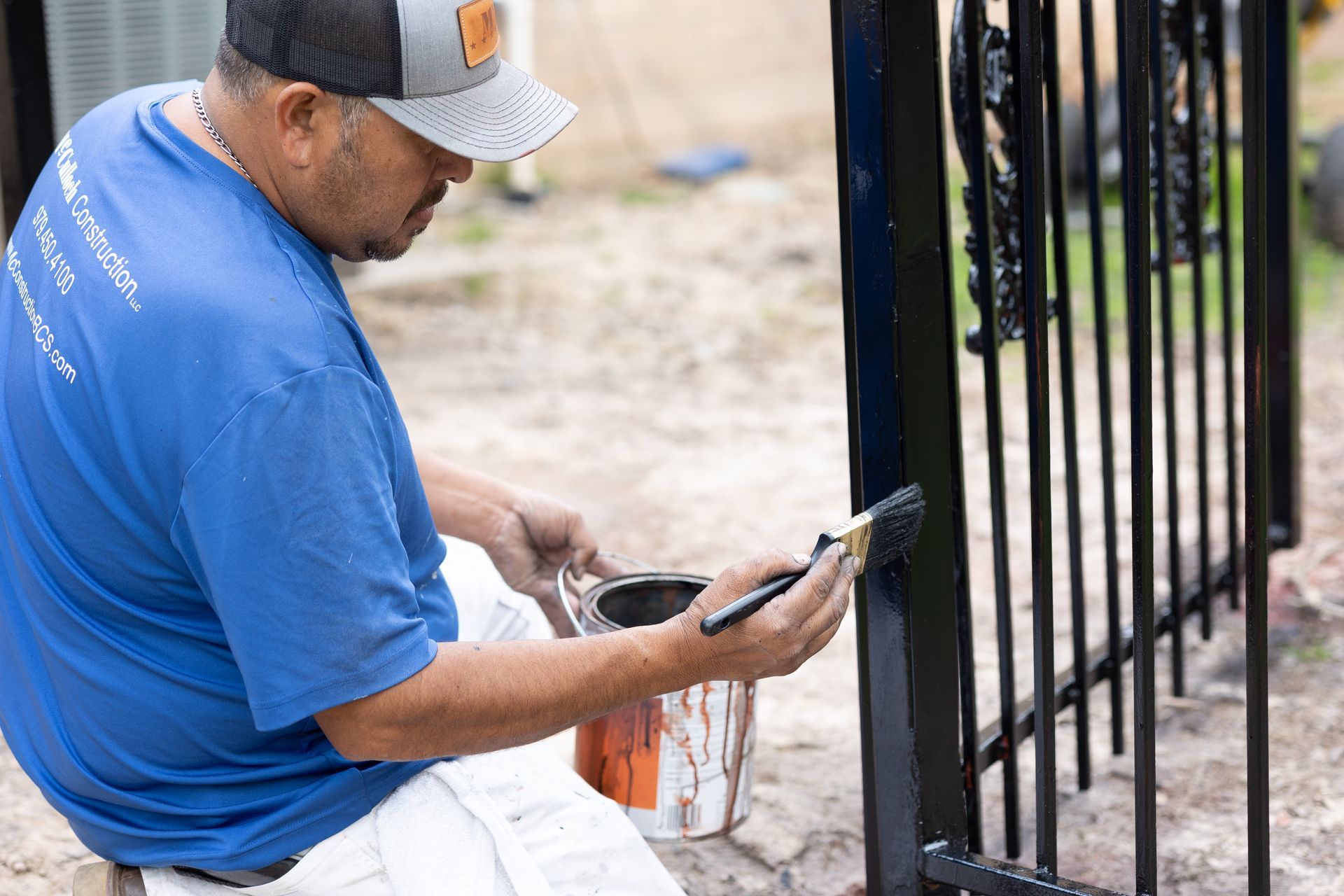 A man is sitting on the ground painting a fence with a brush.