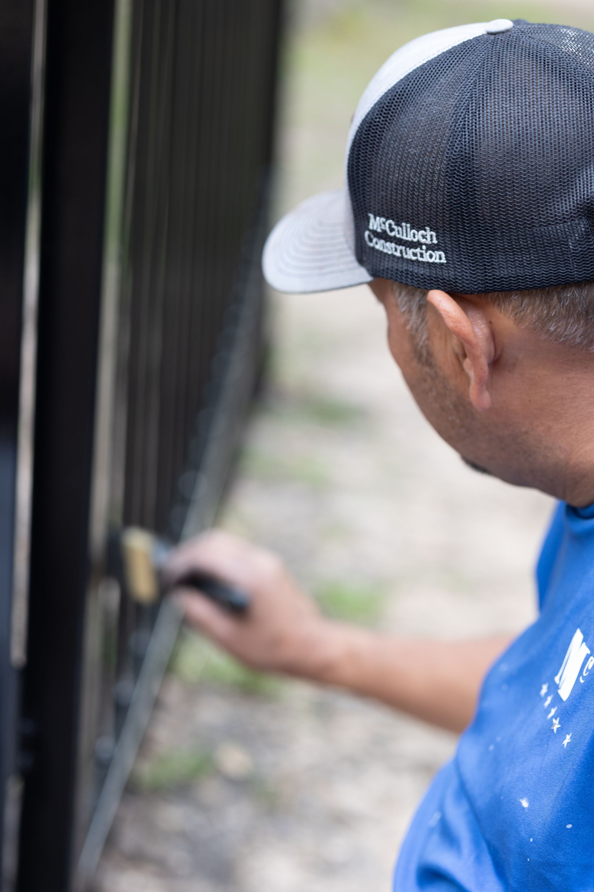 A man wearing a hat is painting a fence with a brush.