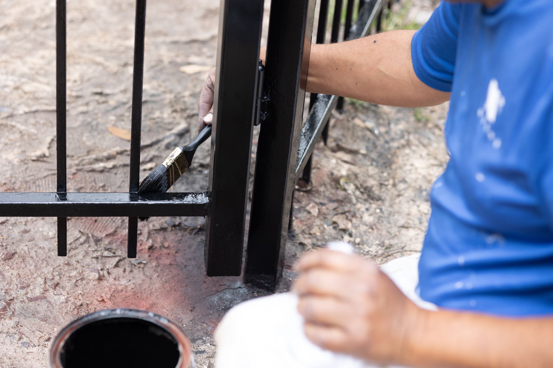 A man is painting a metal fence with a brush.