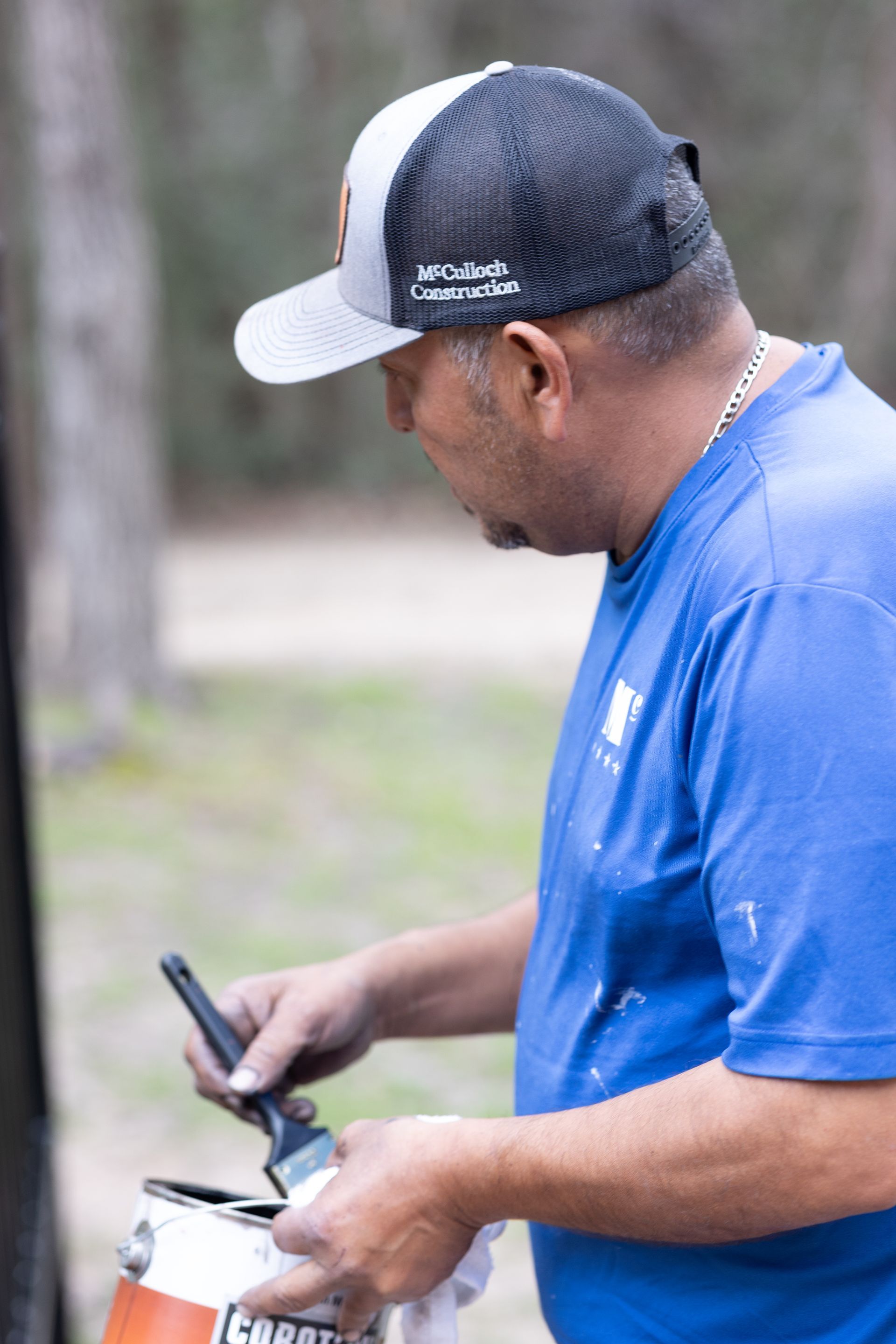 A man in a blue shirt is holding a can of paint and a cell phone.