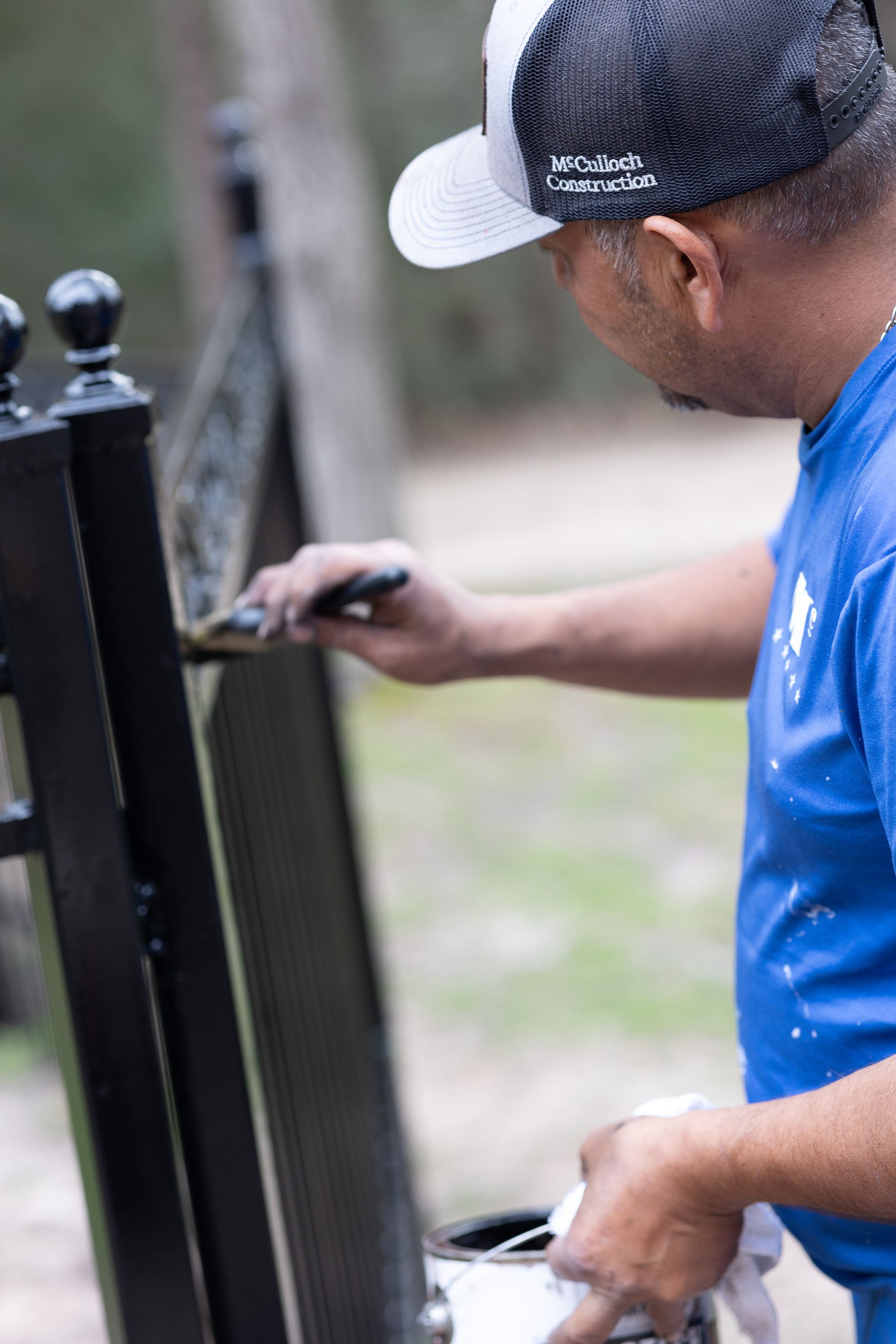 A man in a blue shirt is painting a fence with a brush.