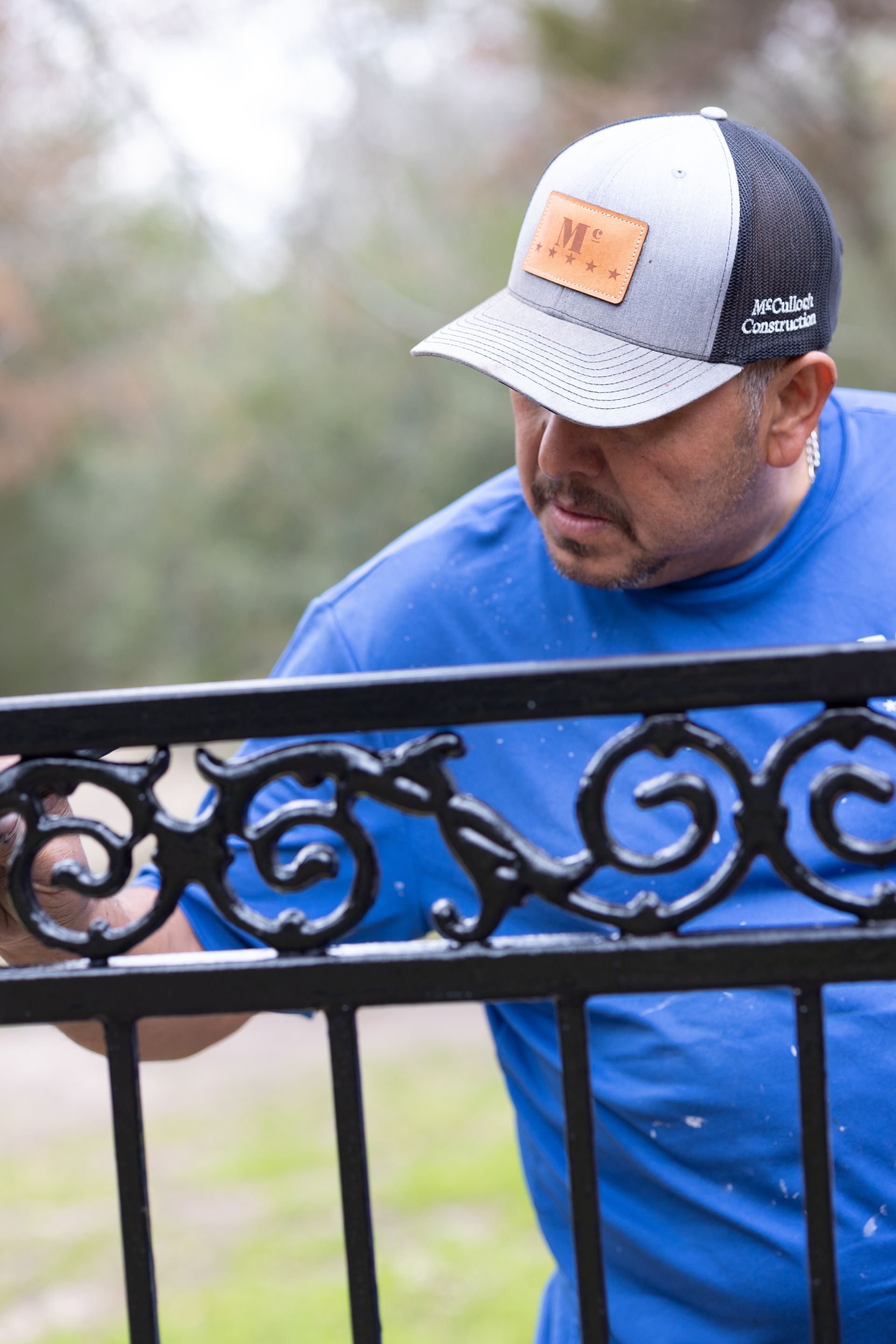 A man in a blue shirt and hat is painting a fence