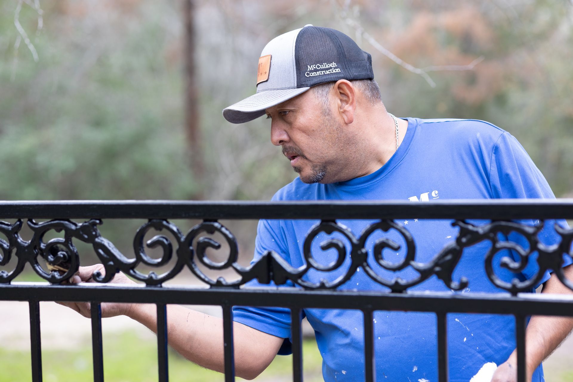 A man in a blue shirt is painting a metal fence.