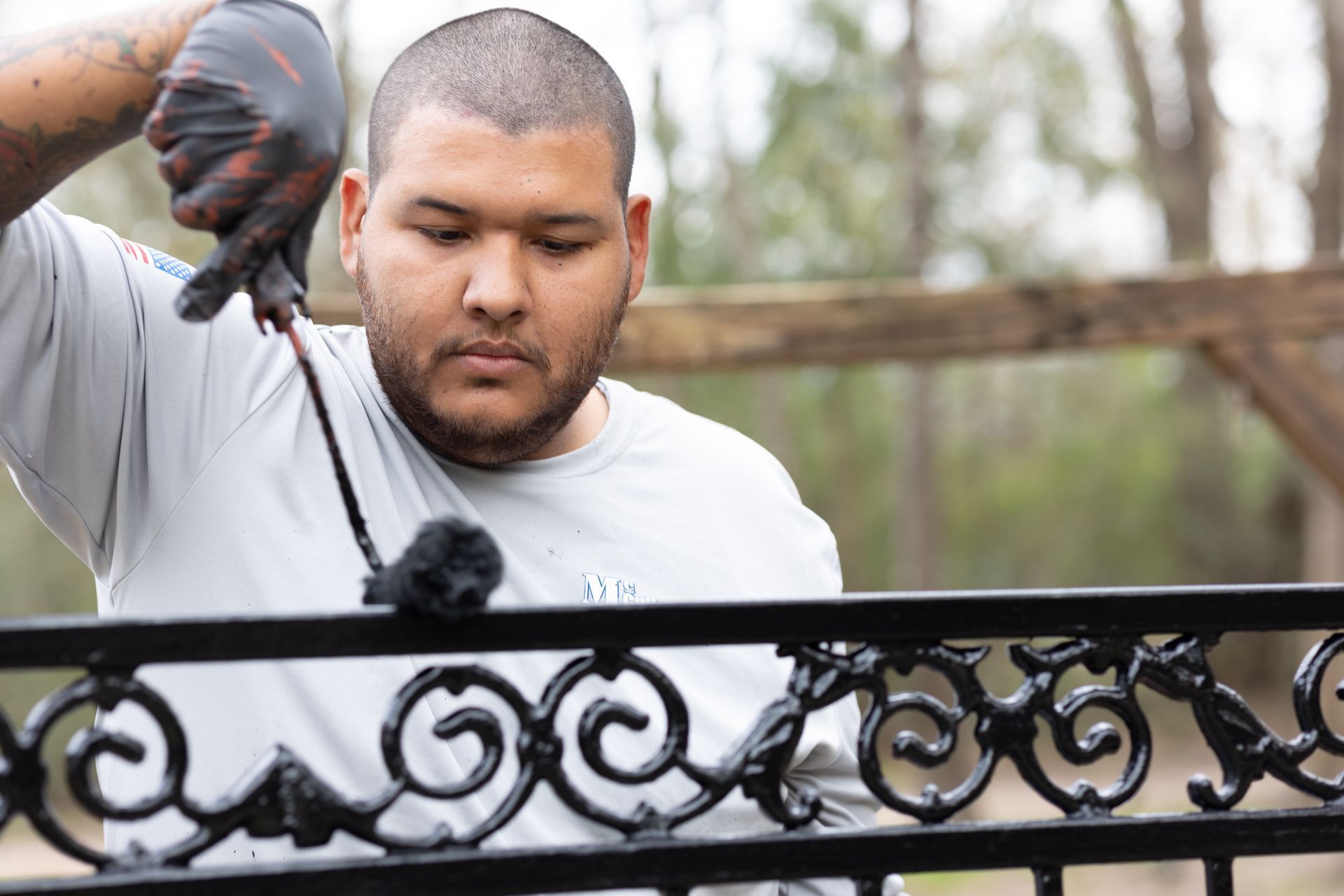A man is painting a wrought iron fence with black paint.