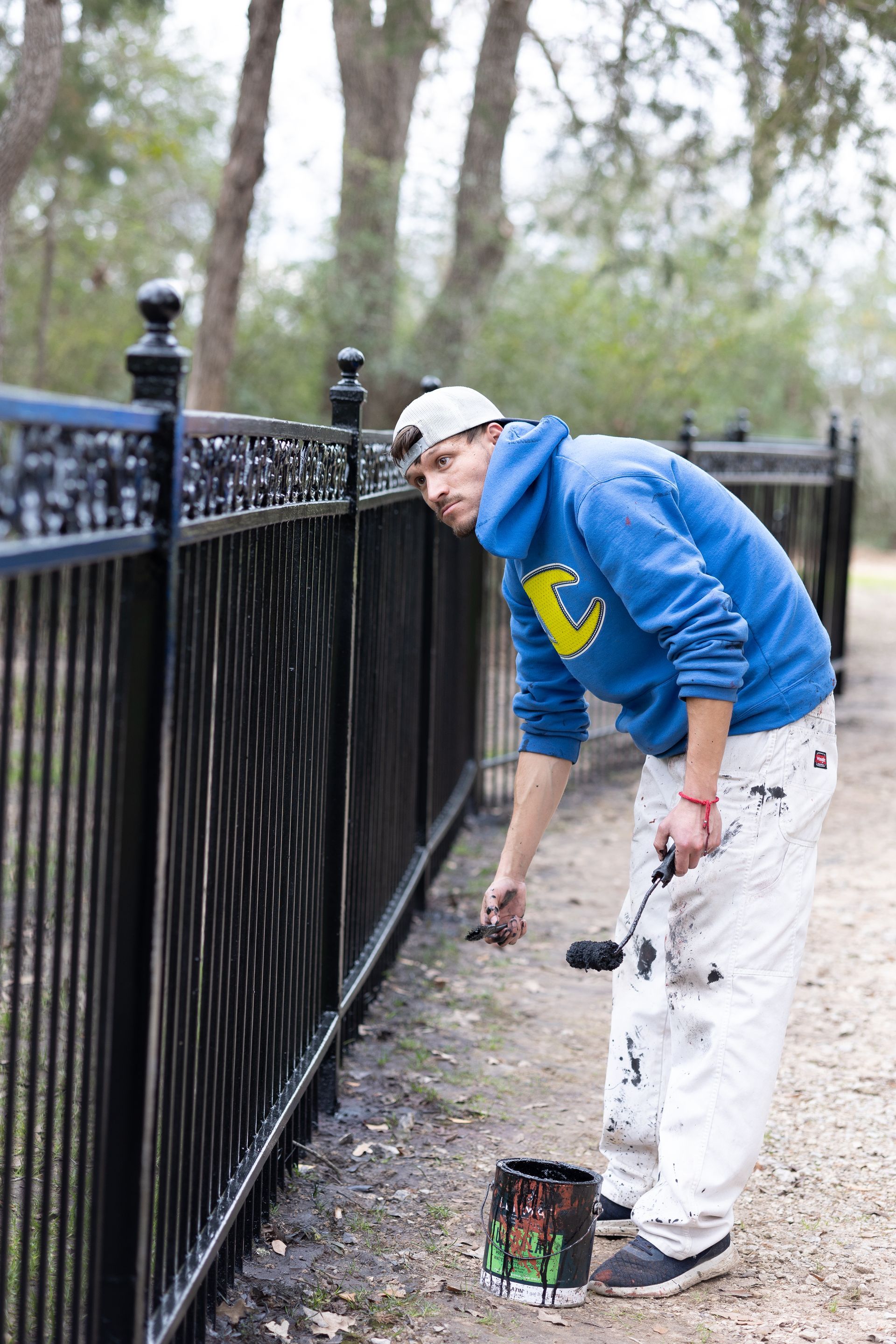 A man in a blue hoodie is painting a black fence.