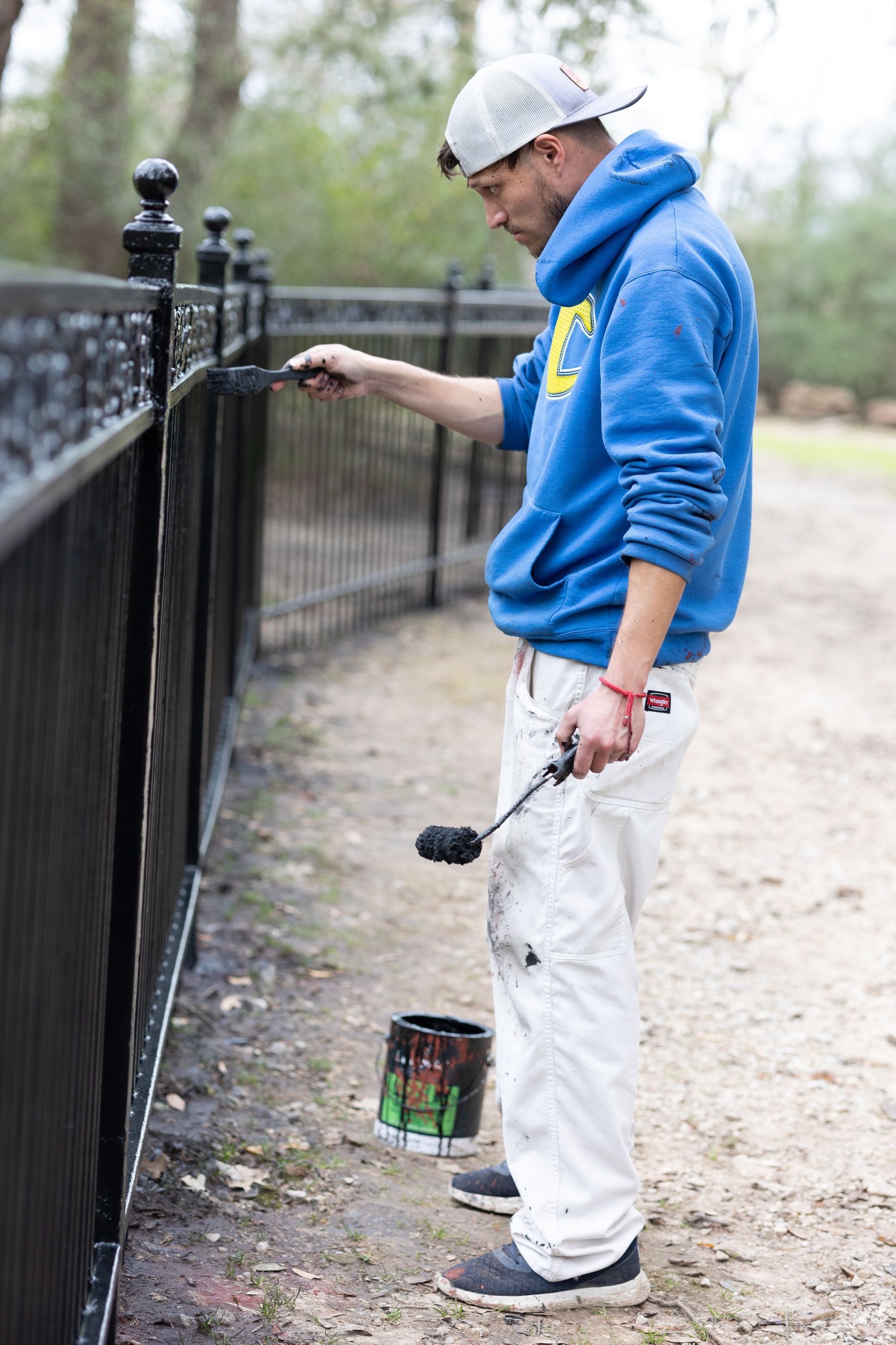 A man is painting a fence with a roller.