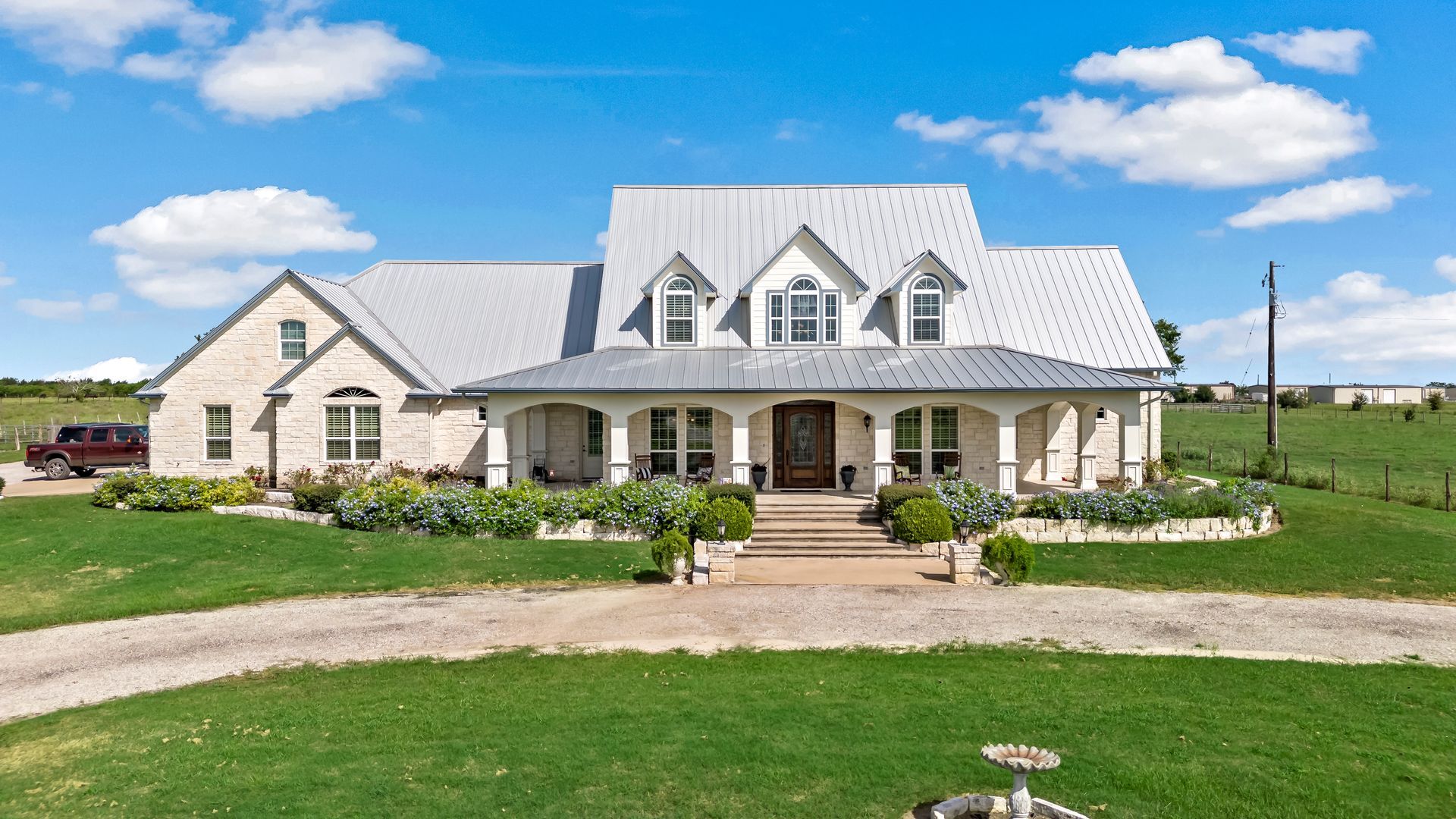 A large white house with a metal roof is sitting on top of a lush green field.