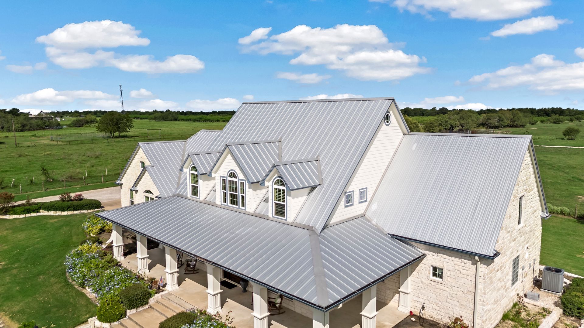 An aerial view of a large white house with a metal roof in the middle of a grassy field.