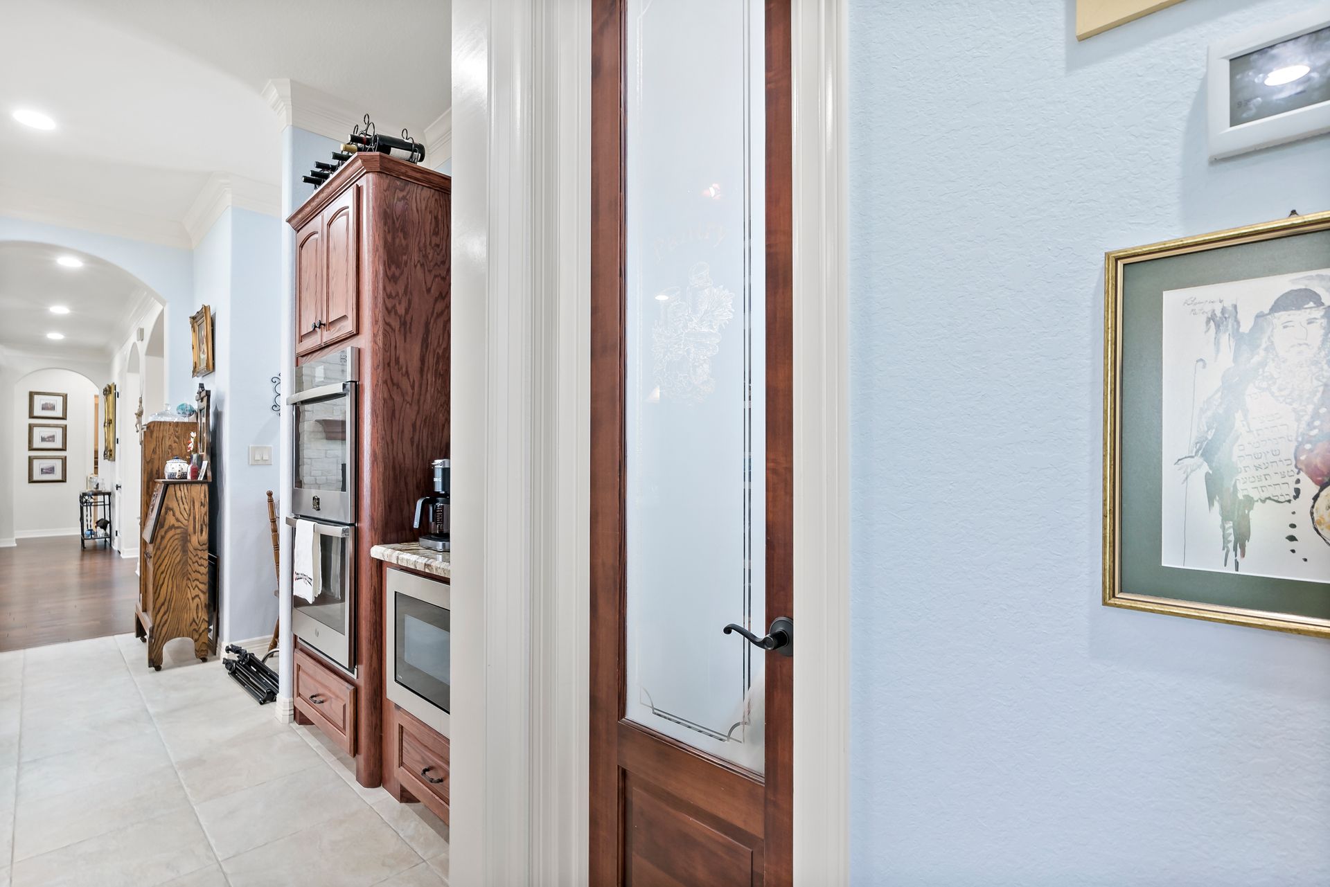 A hallway leading to a kitchen with a picture on the wall.
