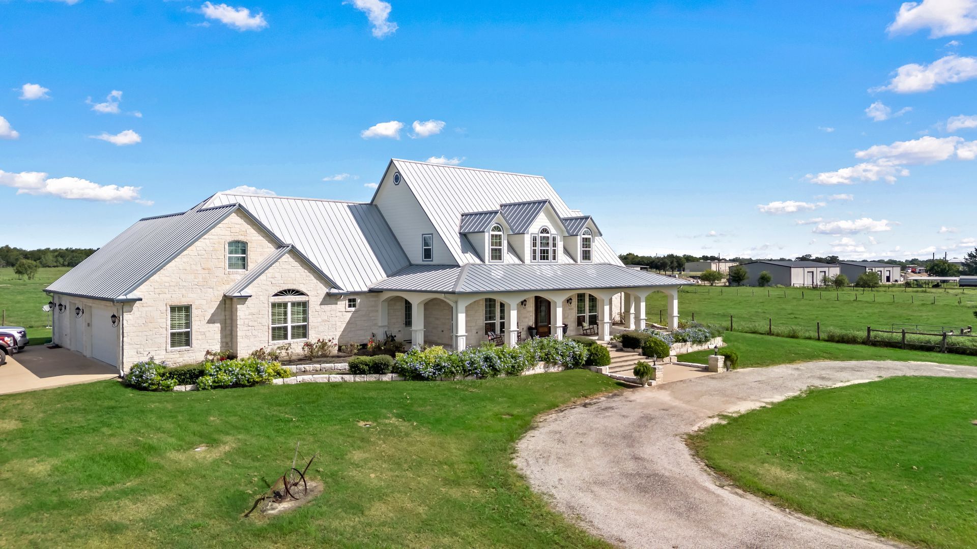 A large white house with a metal roof is sitting on top of a lush green field.