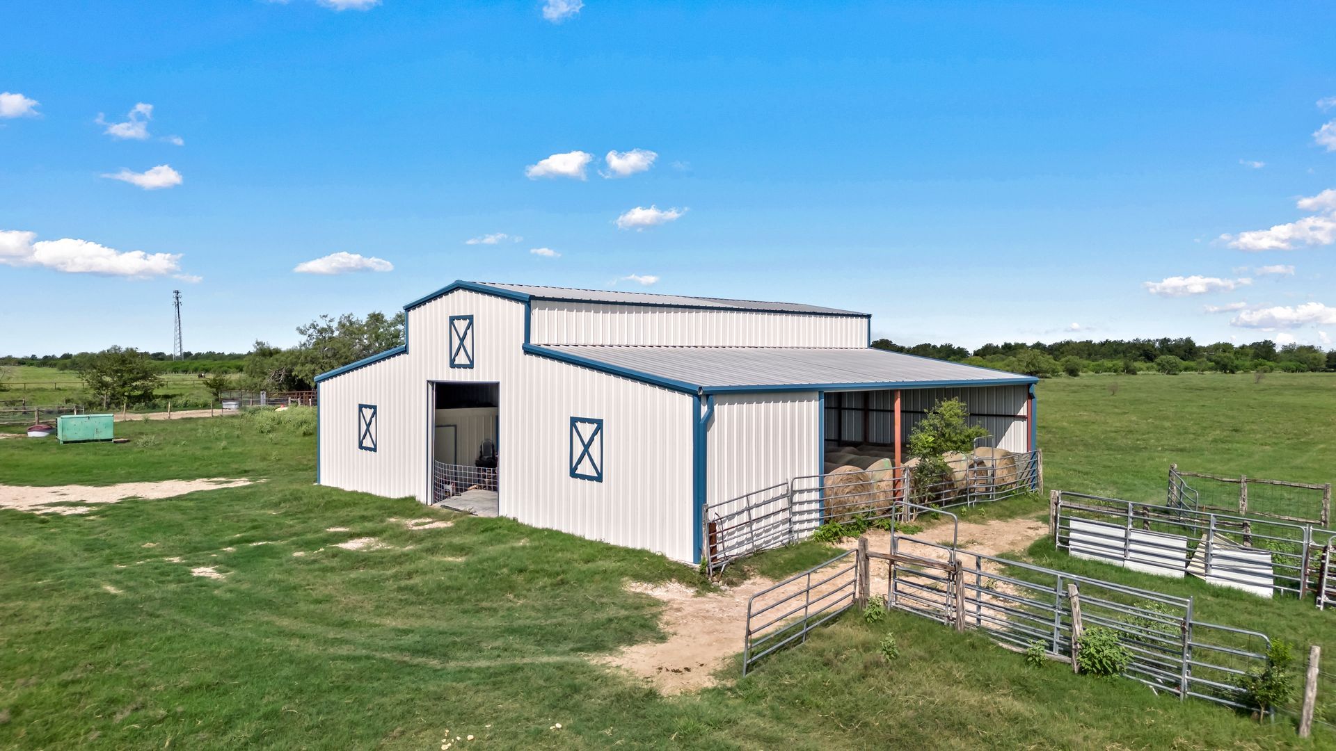 An aerial view of a white barn in the middle of a grassy field.