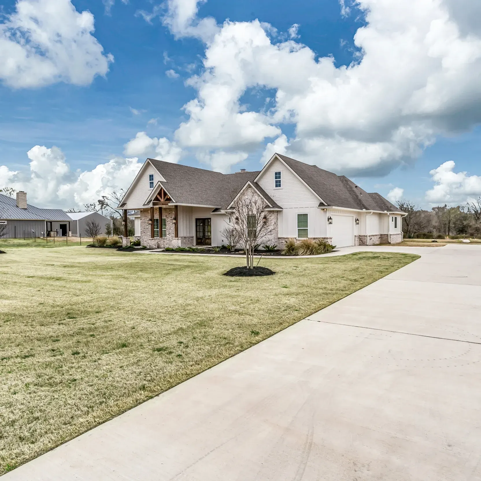 A large white house with a gray roof is sitting on top of a lush green field.