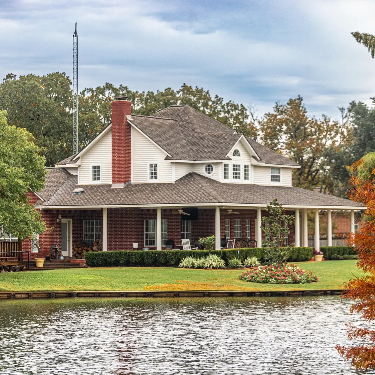 A large house with a large porch sits next to a body of water