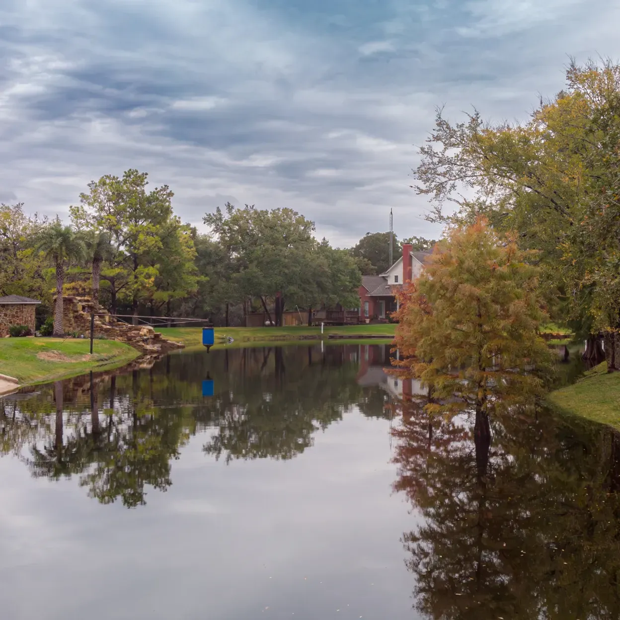 A lake surrounded by trees and grass with a house in the background