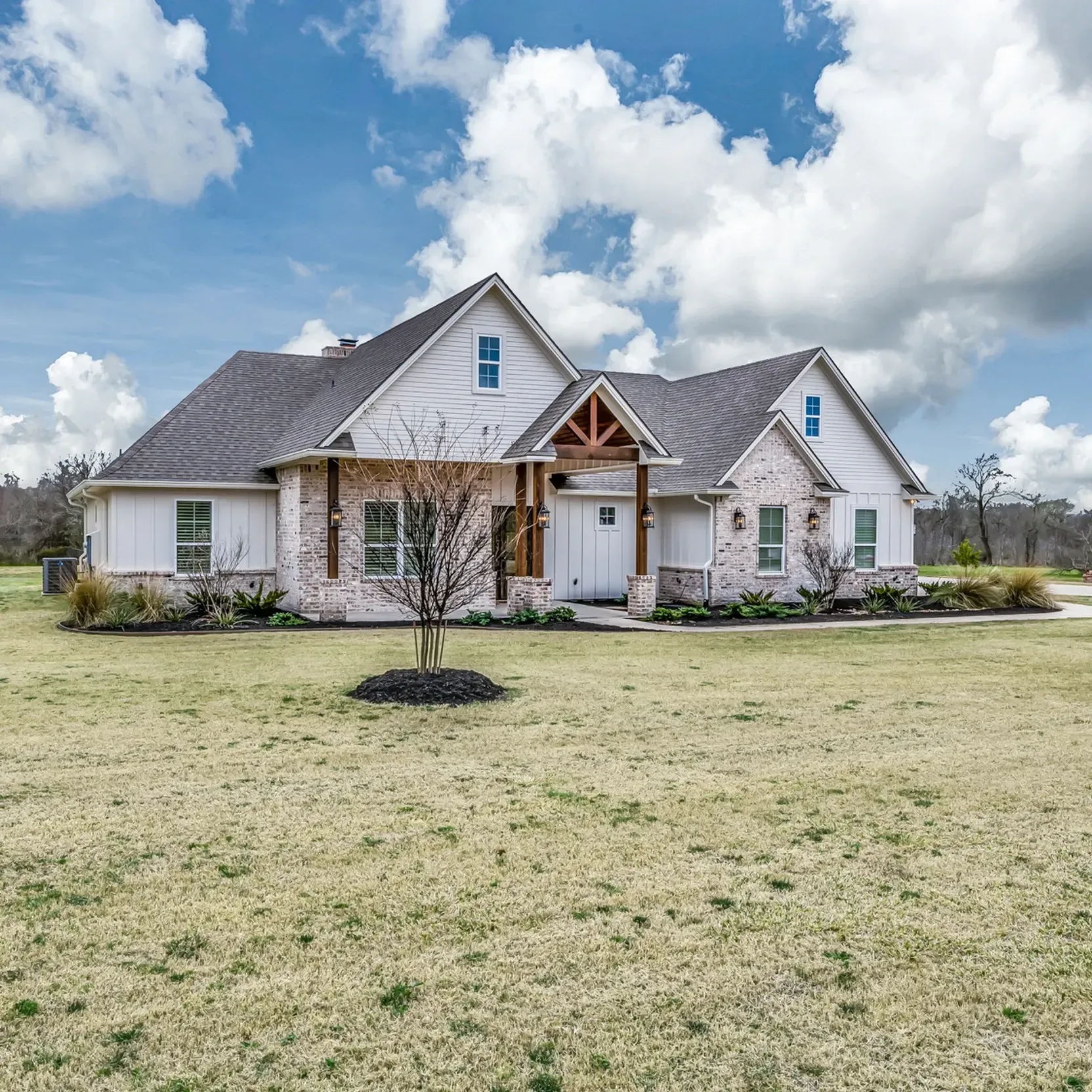 A large white house with a gray roof is sitting in the middle of a grassy field.