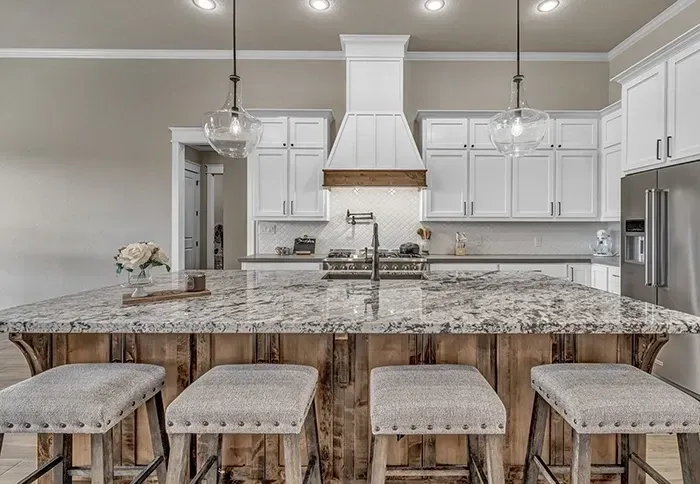 A kitchen with white cabinets , granite counter tops , and stools.
