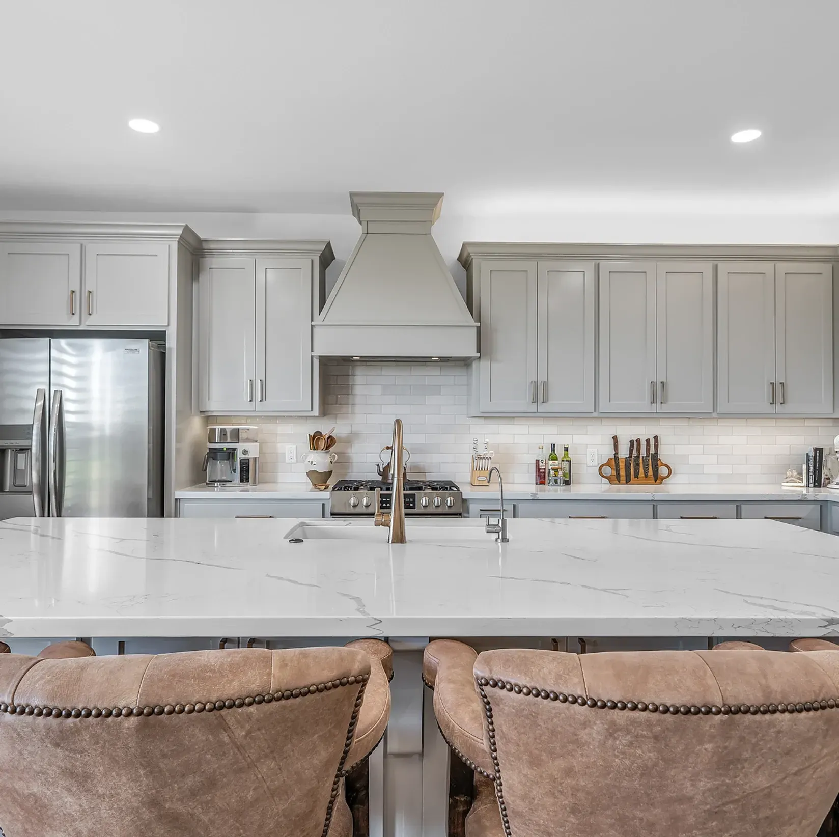 A kitchen with white cabinets , a stove , a refrigerator , a sink , and a large island.