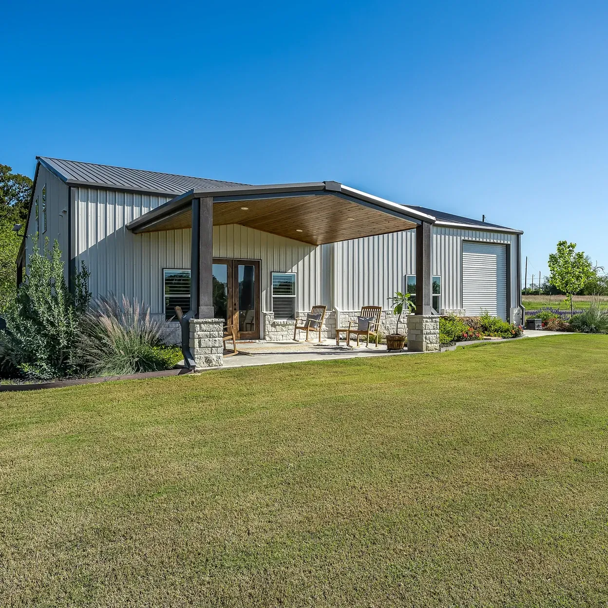A small house with a porch and chairs in a grassy field.