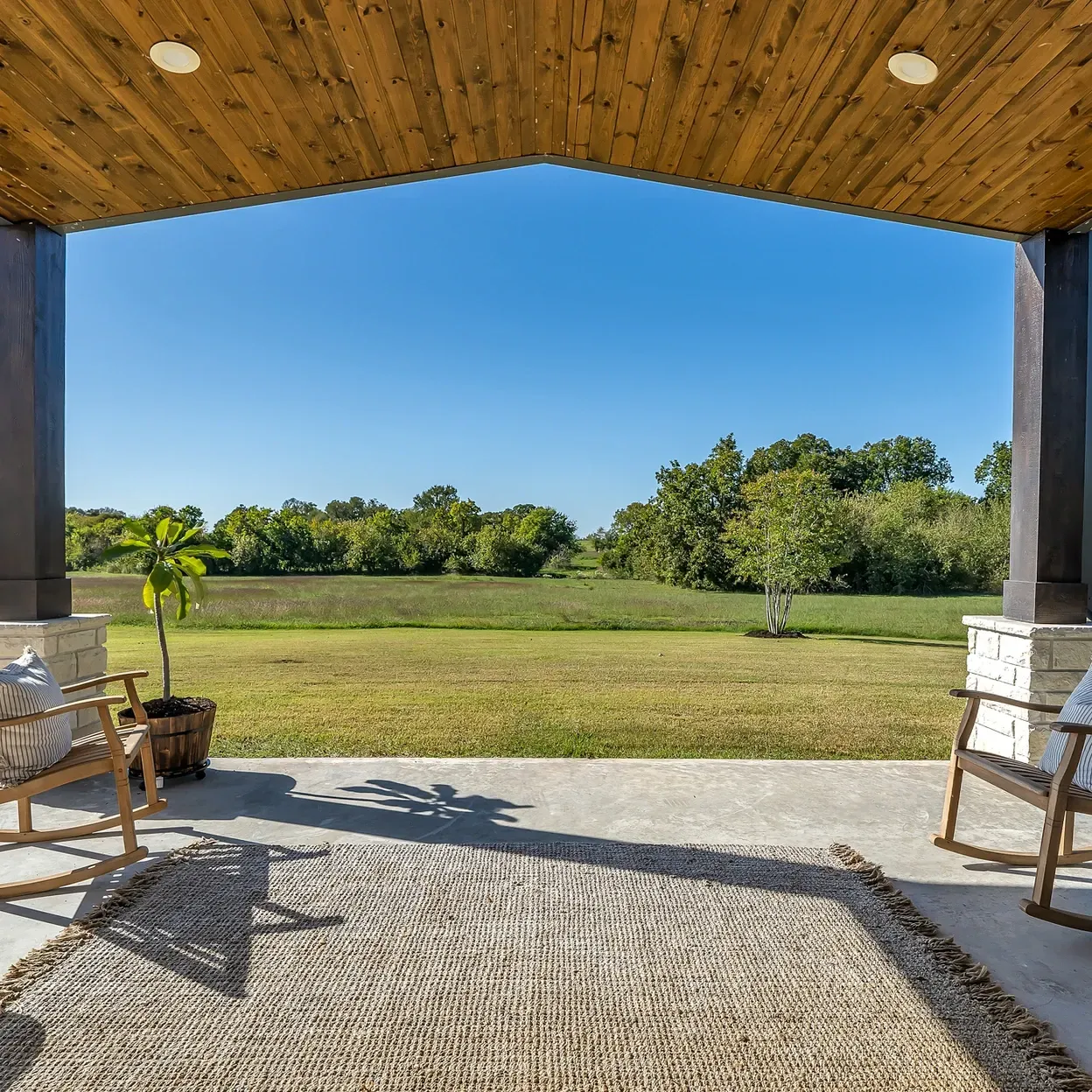 A patio with rocking chairs and a rug and a view of a field.