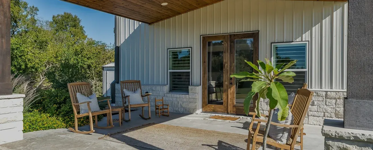 A patio with rocking chairs and a plant in front of a house.