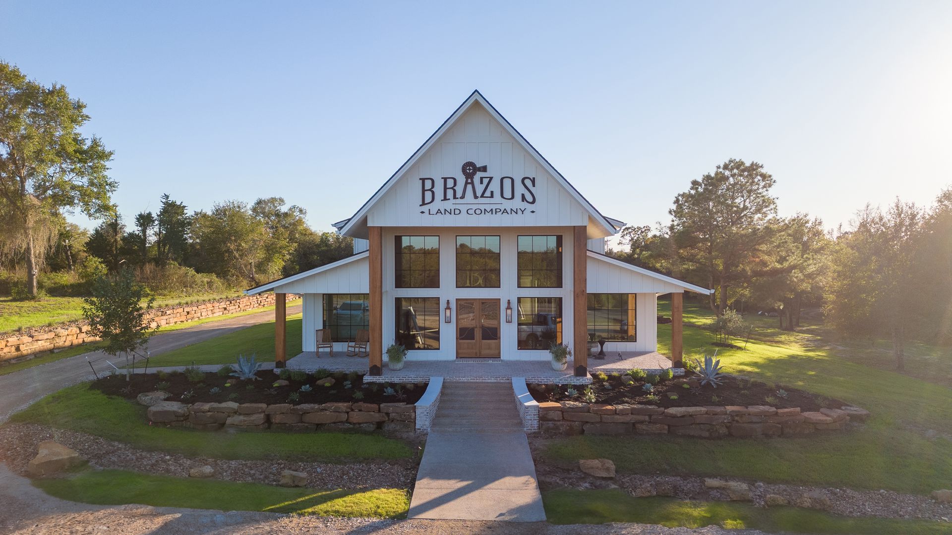 An aerial view of a large white building with a porch and trees in the background.