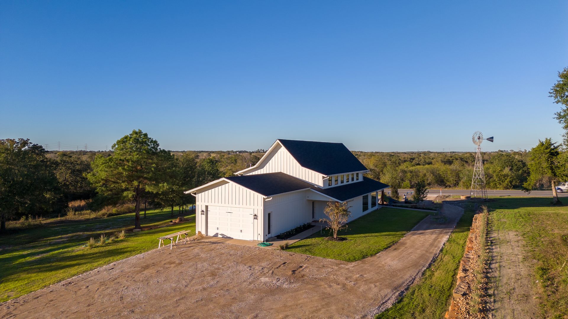 An aerial view of a white house with a black roof and a dirt road leading to it.
