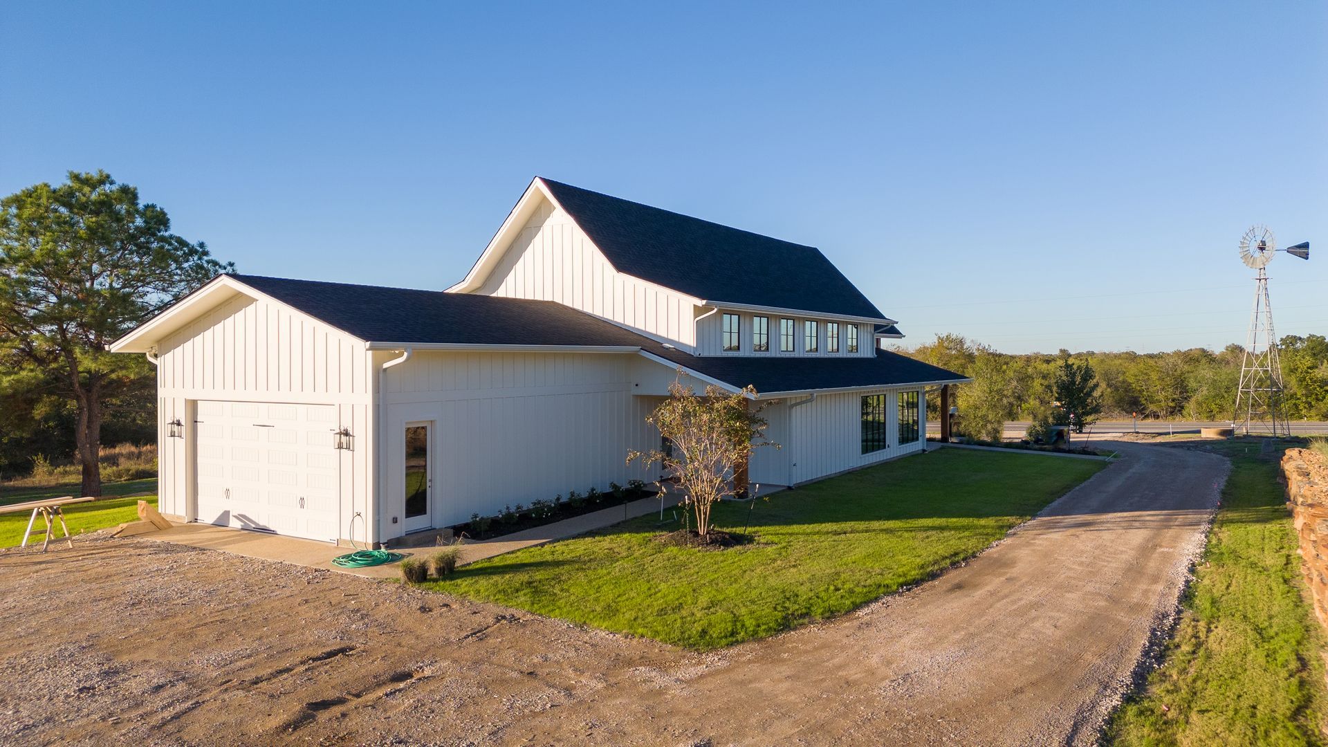 A large white house with a black roof is sitting next to a dirt road.