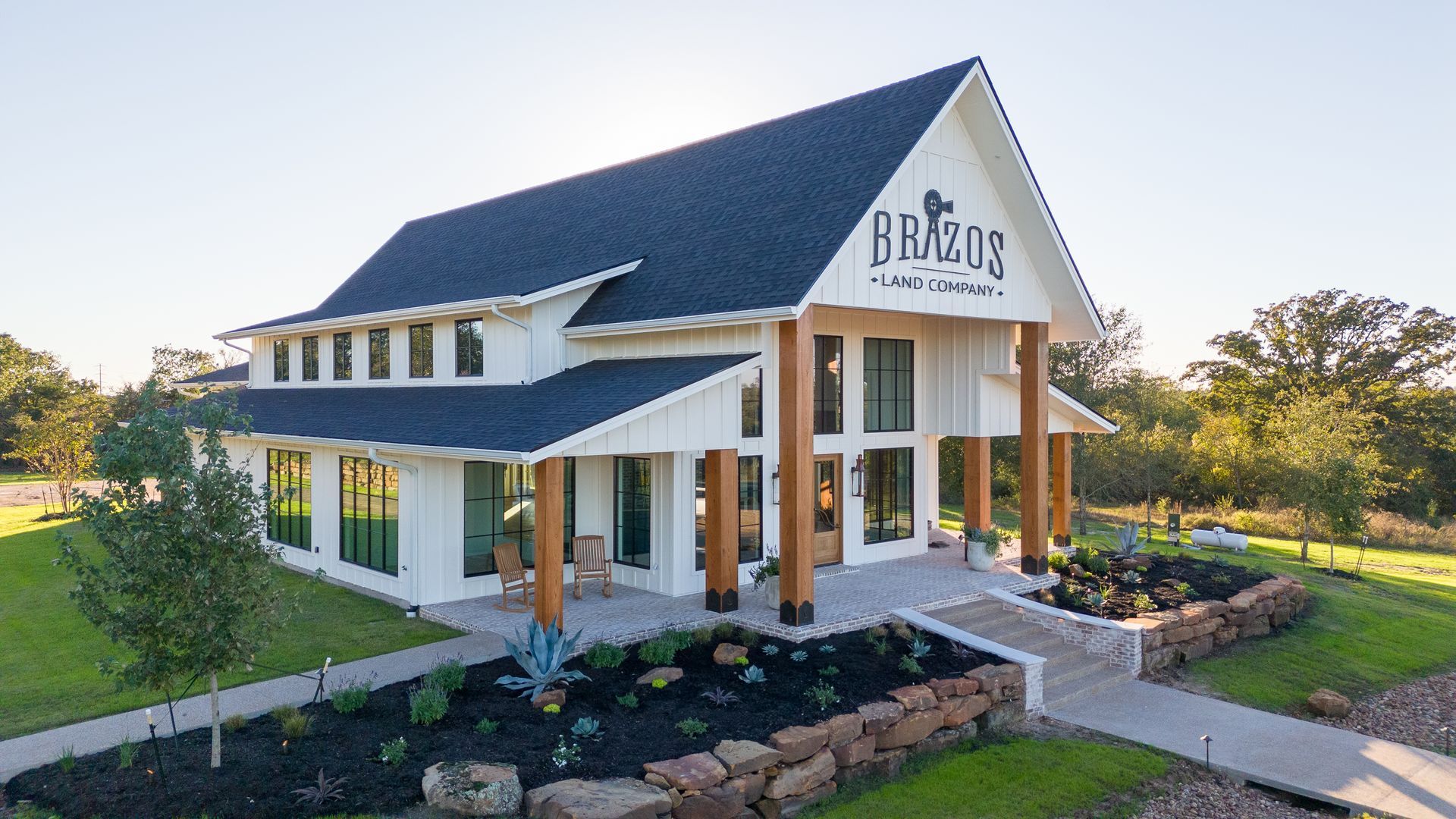 A large white house with a black roof is sitting on top of a lush green field.