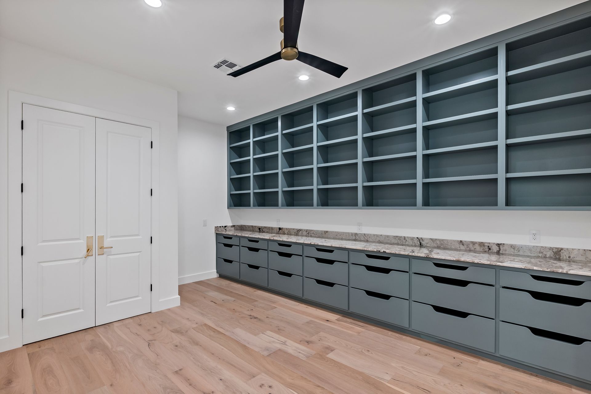 A room with a lot of shelves and drawers and a ceiling fan.