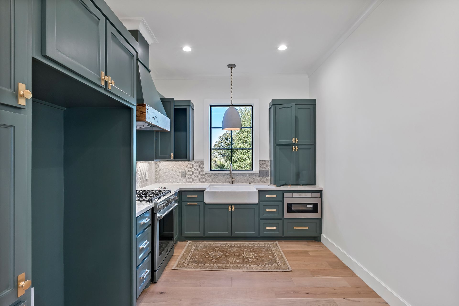 A kitchen with green cabinets , stainless steel appliances , a sink and a window.