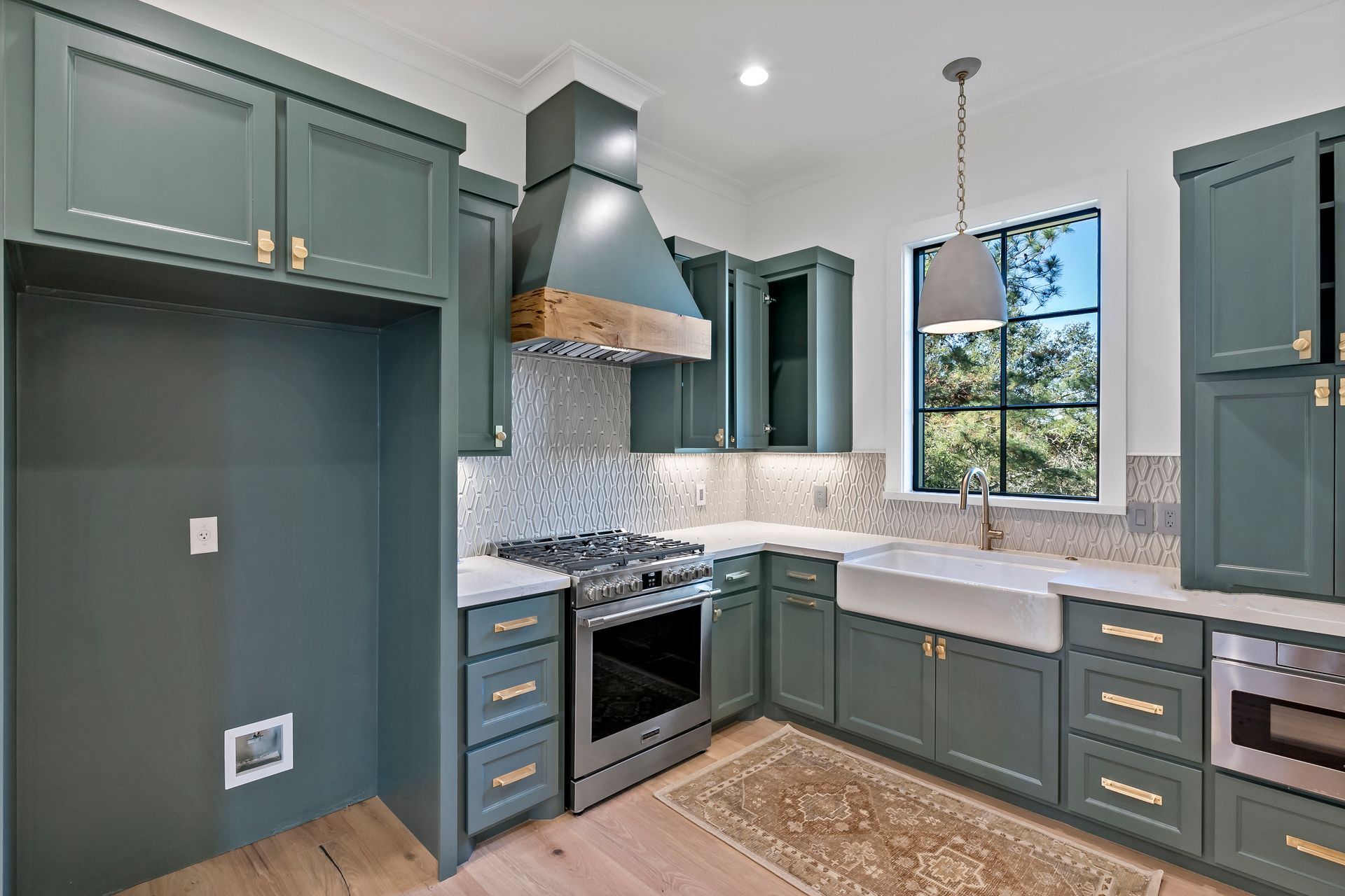 A kitchen with green cabinets , a stove , a sink , and a window.