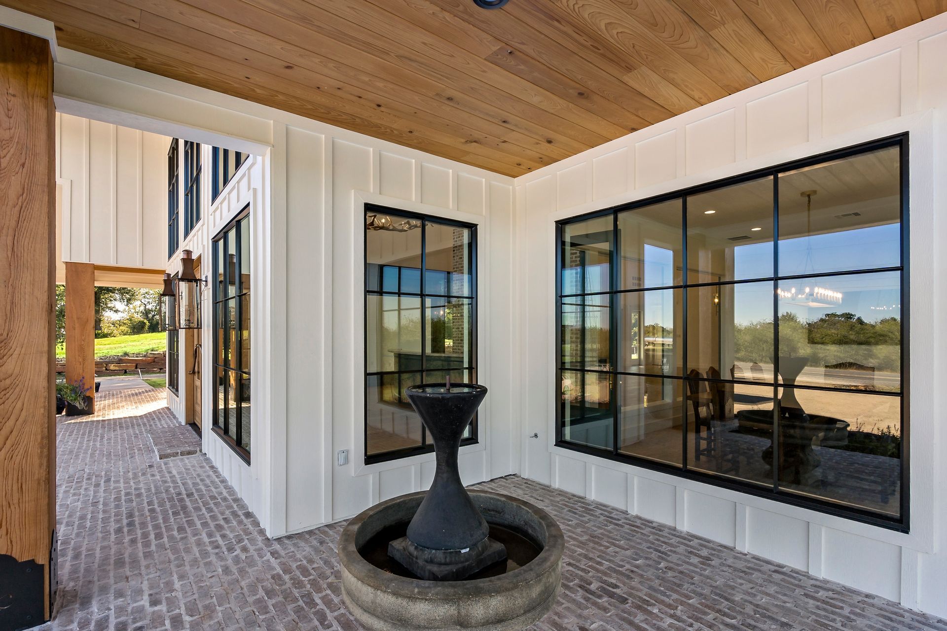 Entryway with brick floor, white walls, black-framed windows, wood ceiling, and a fountain.