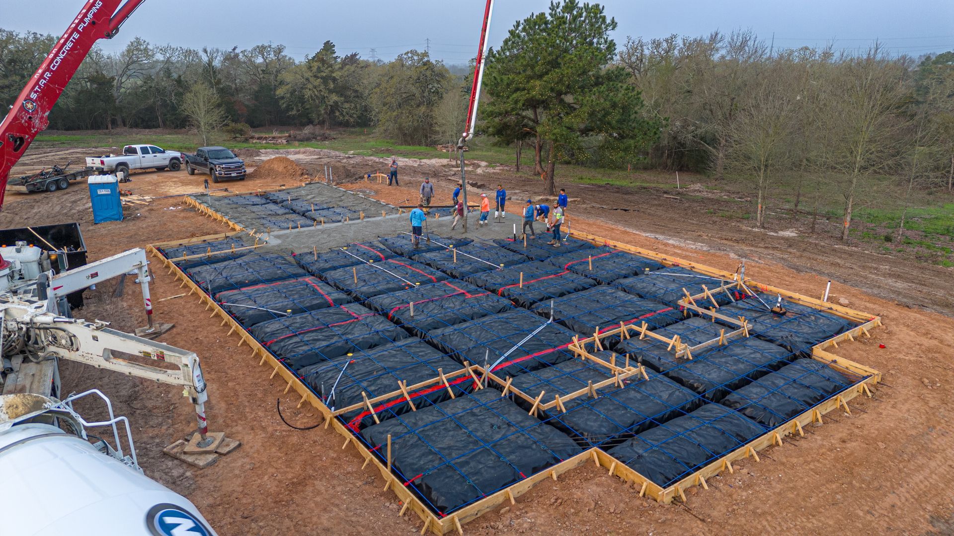 An aerial view of a concrete foundation being poured by a crane.