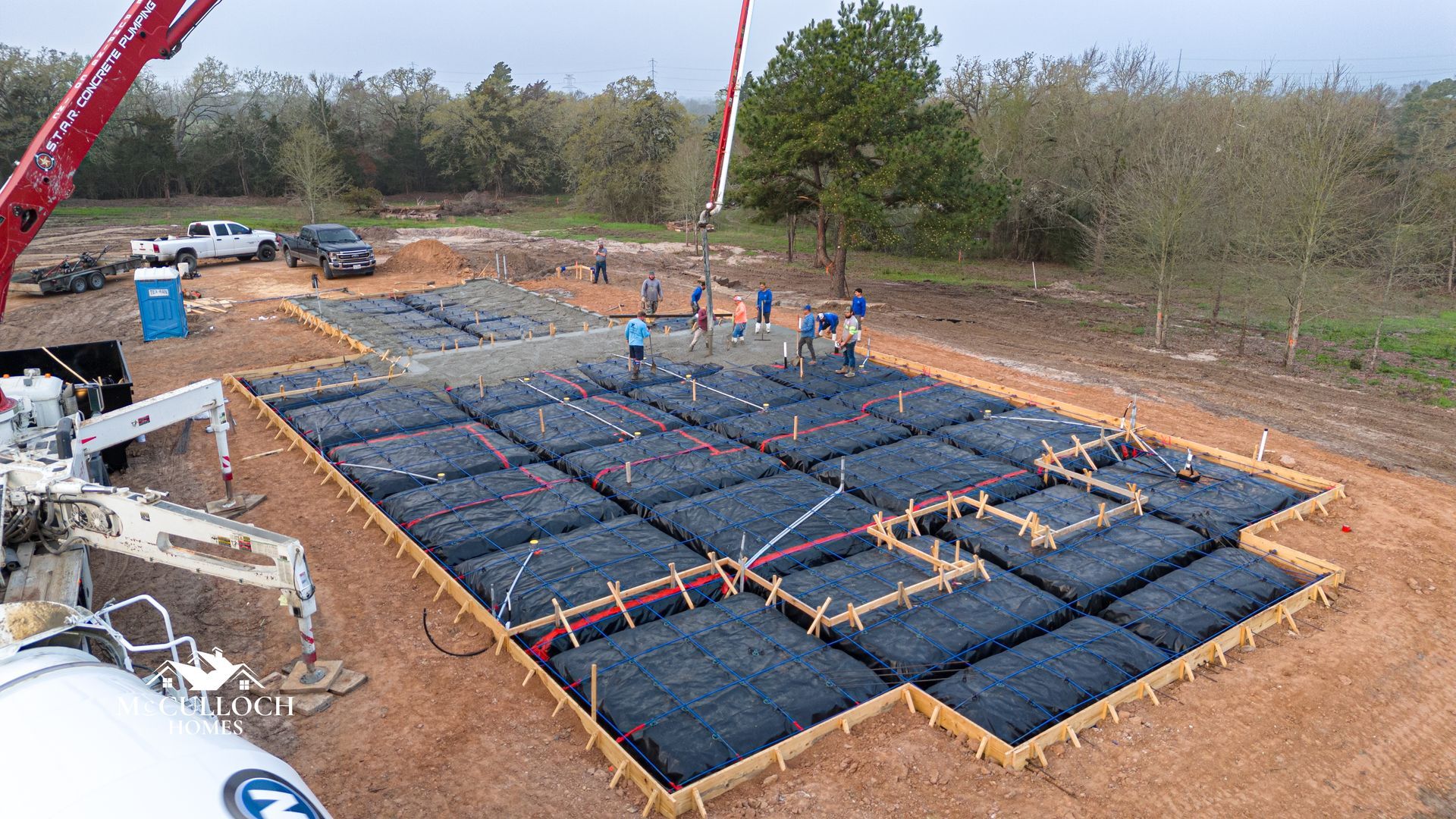 An aerial view of a concrete foundation being poured by a crane.